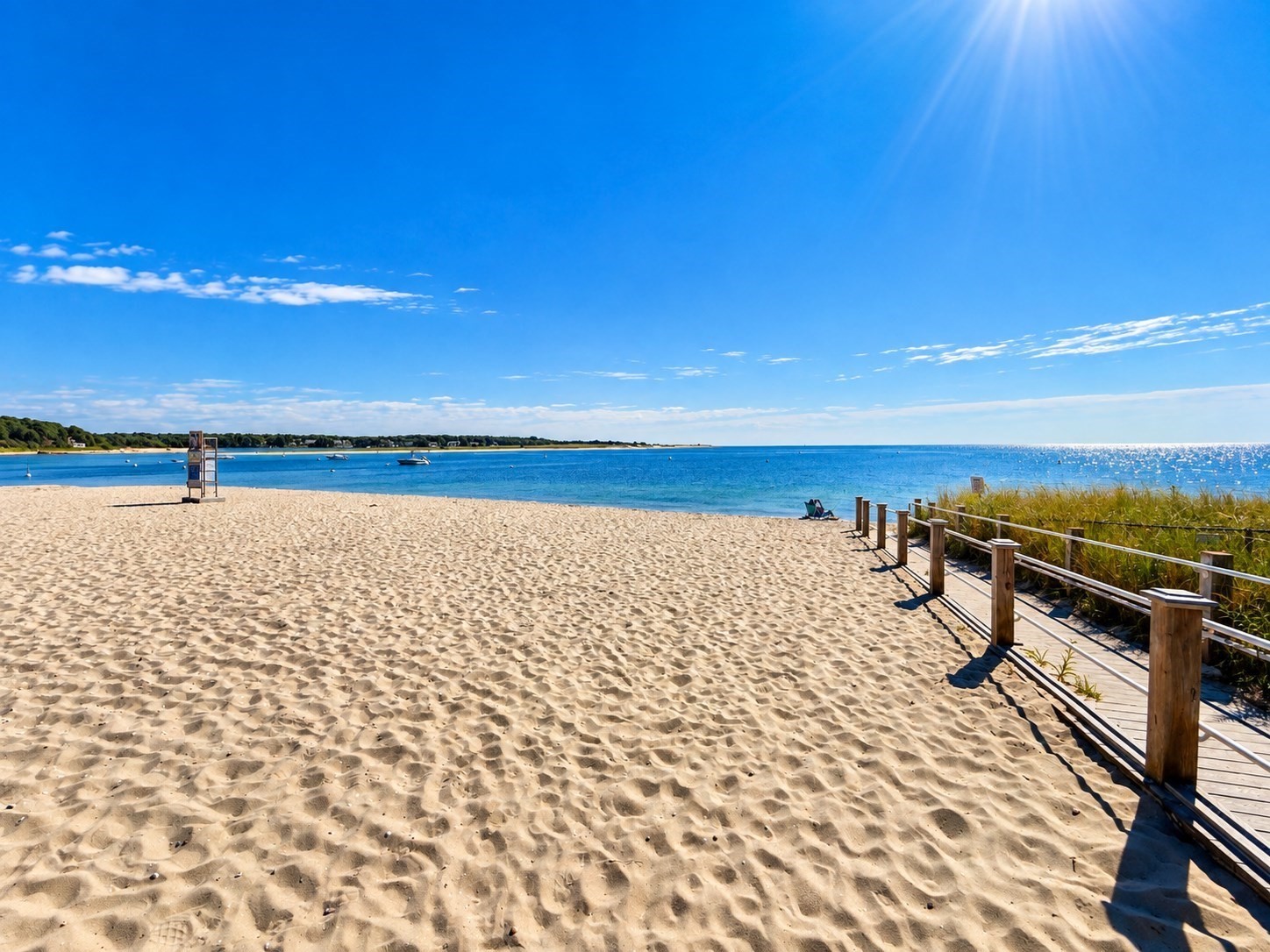 Sandy beach and blue ocean with a wooden boardwalk along the dune grass.