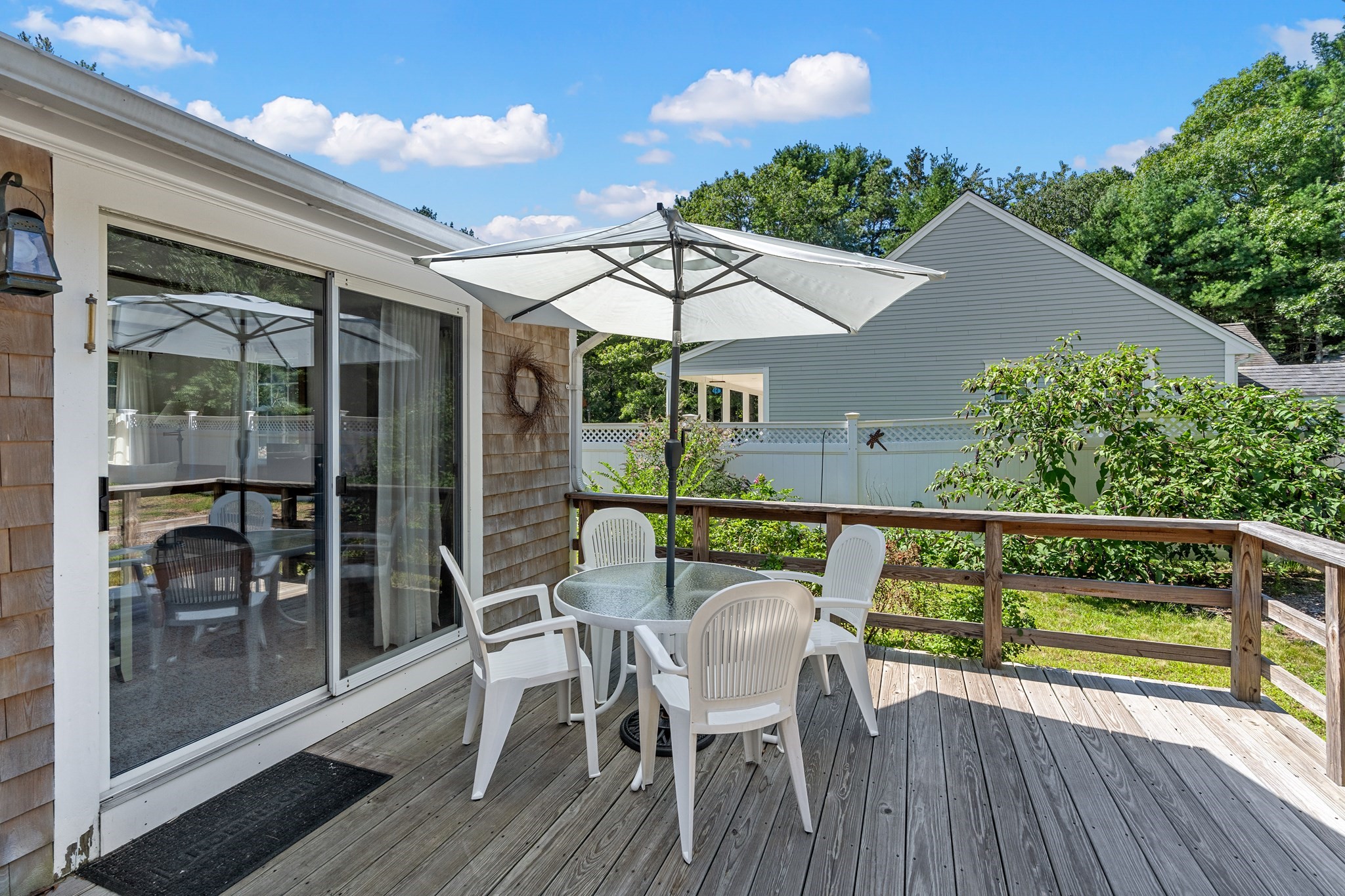 Wooden deck with white patio furniture beneath a large umbrella beside the house.