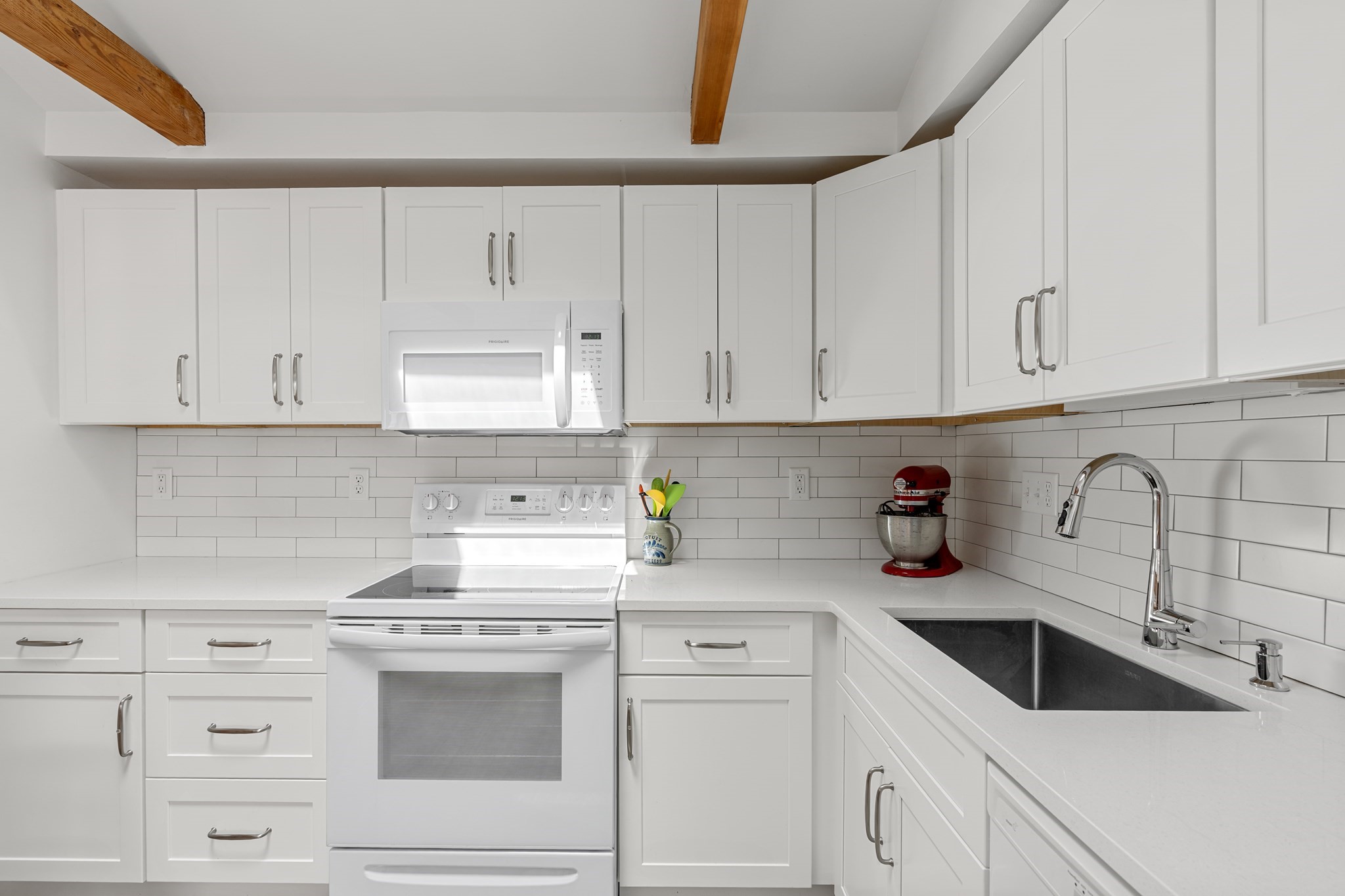 White kitchen with subway tile backsplash, exposed wood beams, and a dark sink with chrome faucet.