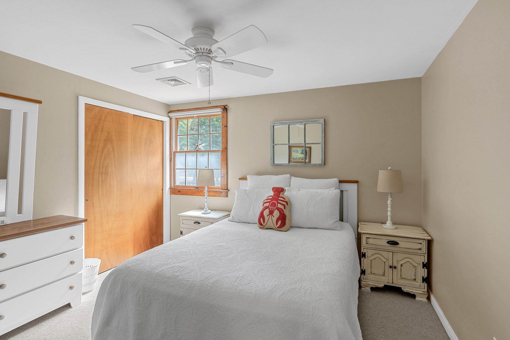 Bedroom with a white quilted bed, red lobster pillow, and wood-trimmed window.