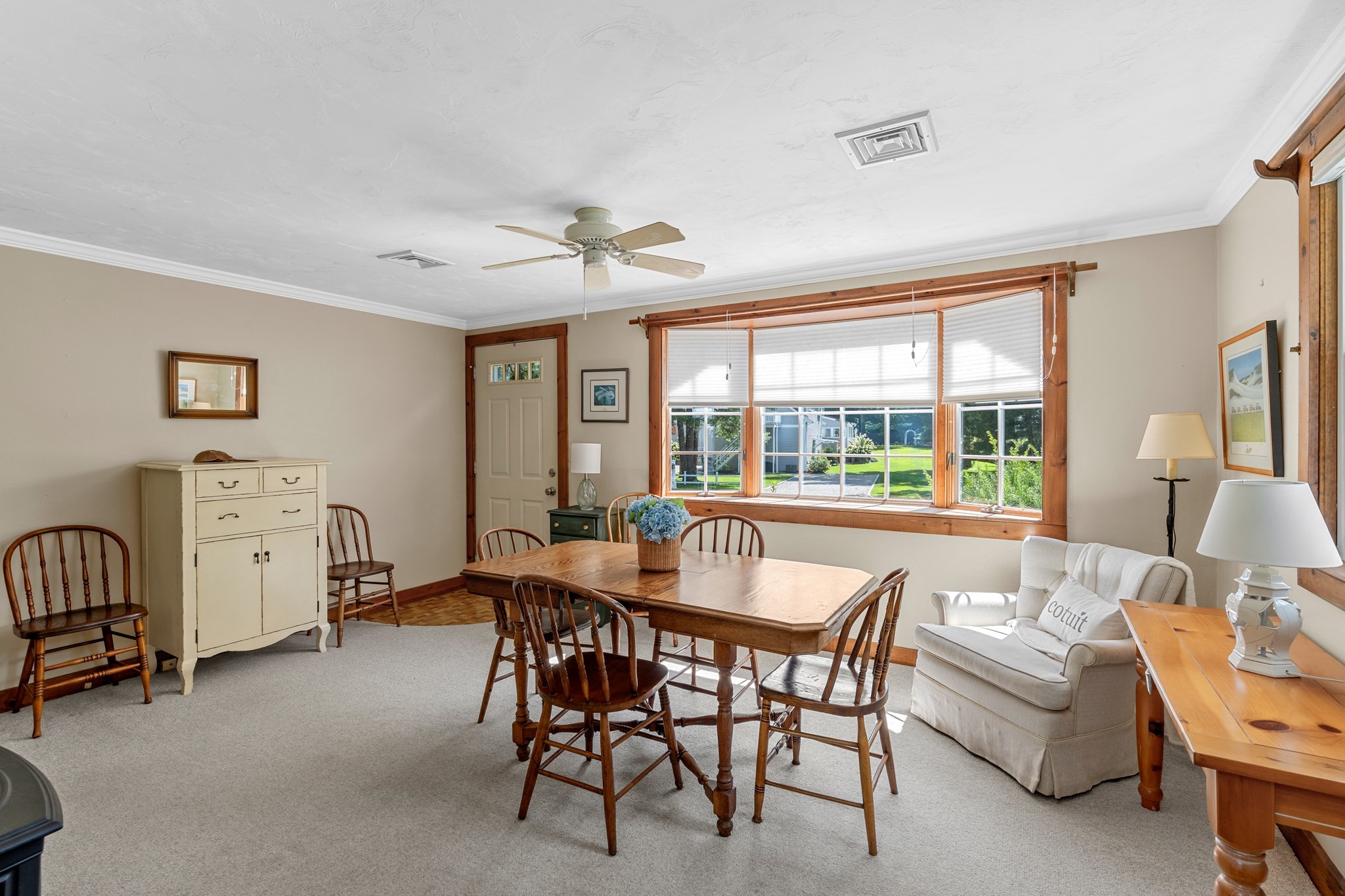 Dining and sitting room with a wooden table and large windows overlooking a green yard.