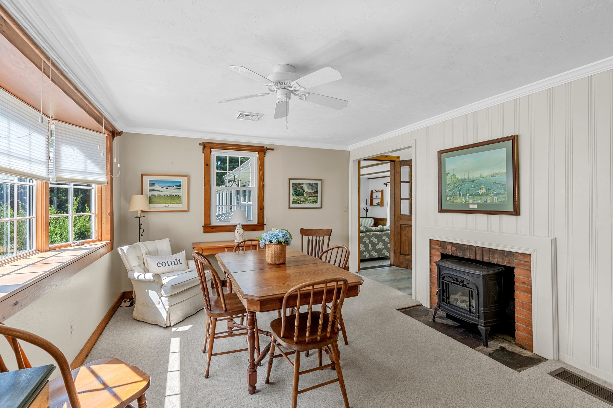 Dining room with a wooden table, sunlit windows, and brick fireplace with a black stove.