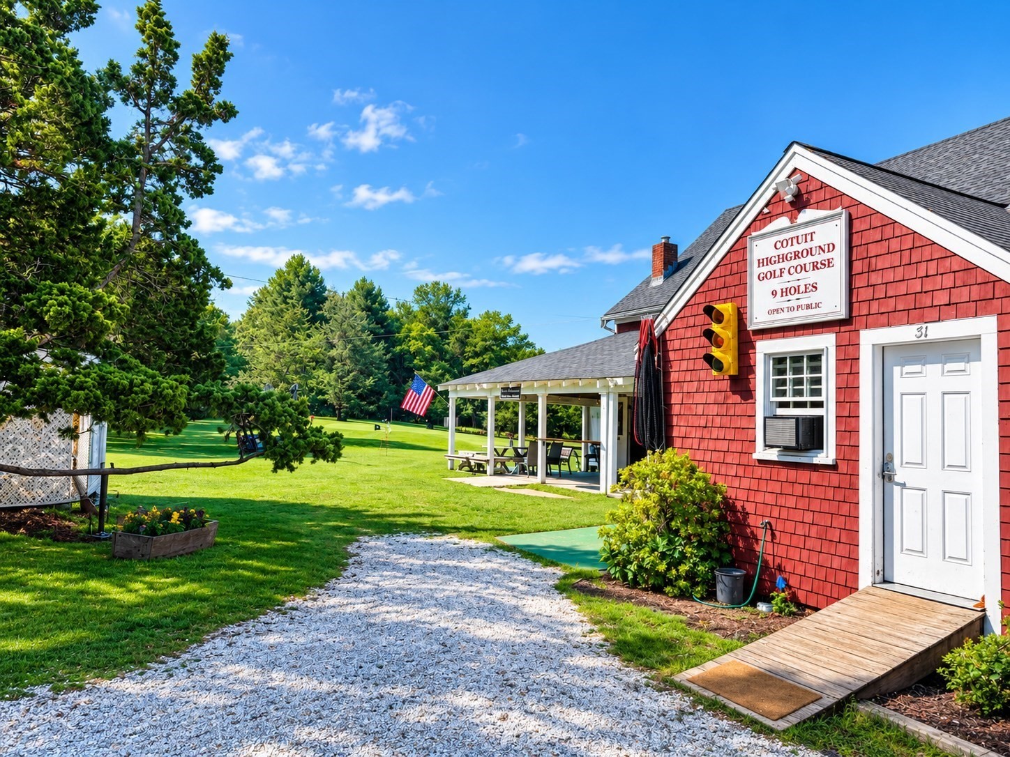 Cotuit Highground Golf Course clubhouse beside a gravel path, with a covered picnic area and flag.