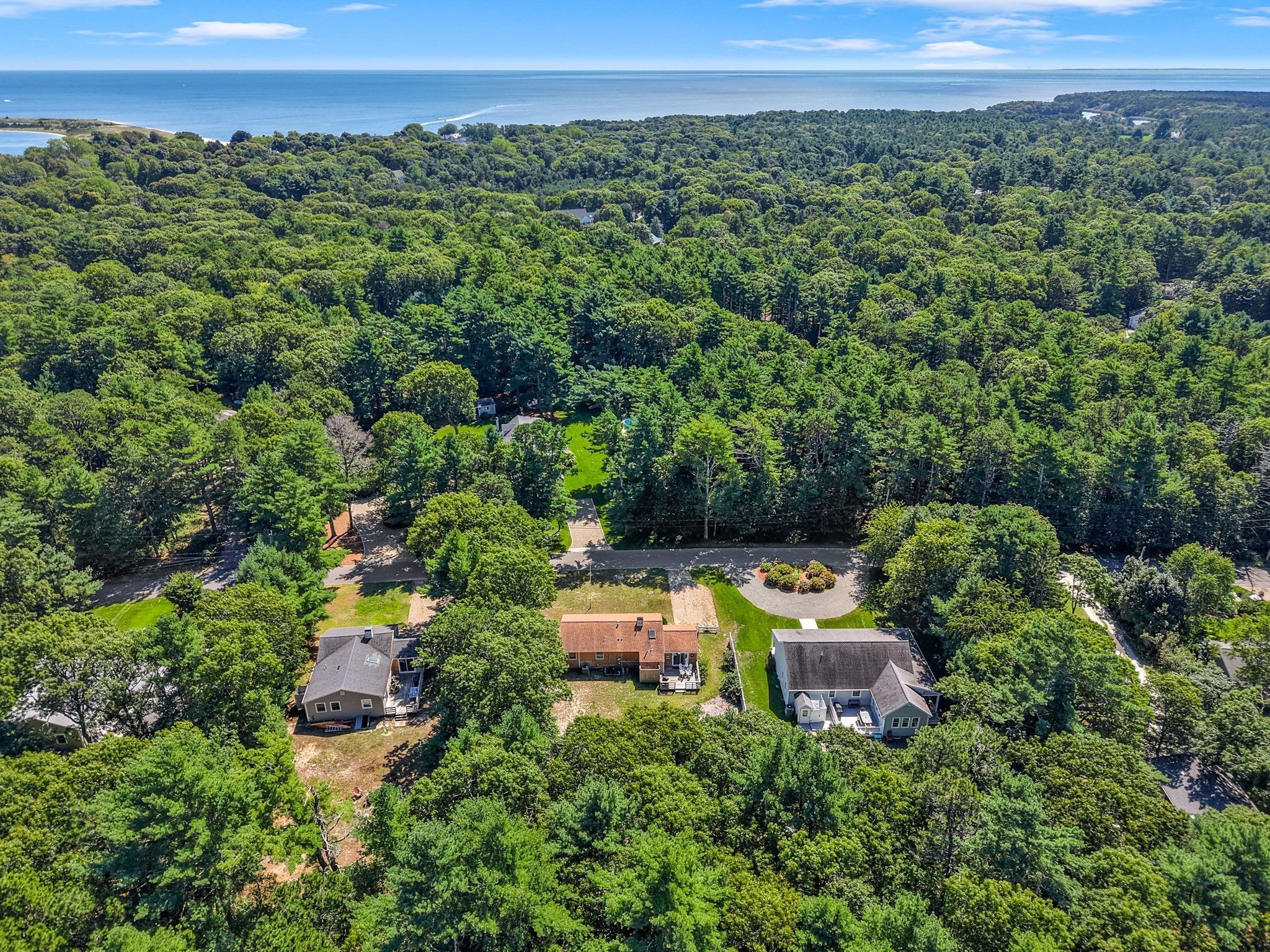 Aerial view of a home surrounded by trees, with the ocean visible beyond the wooded neighborhood.