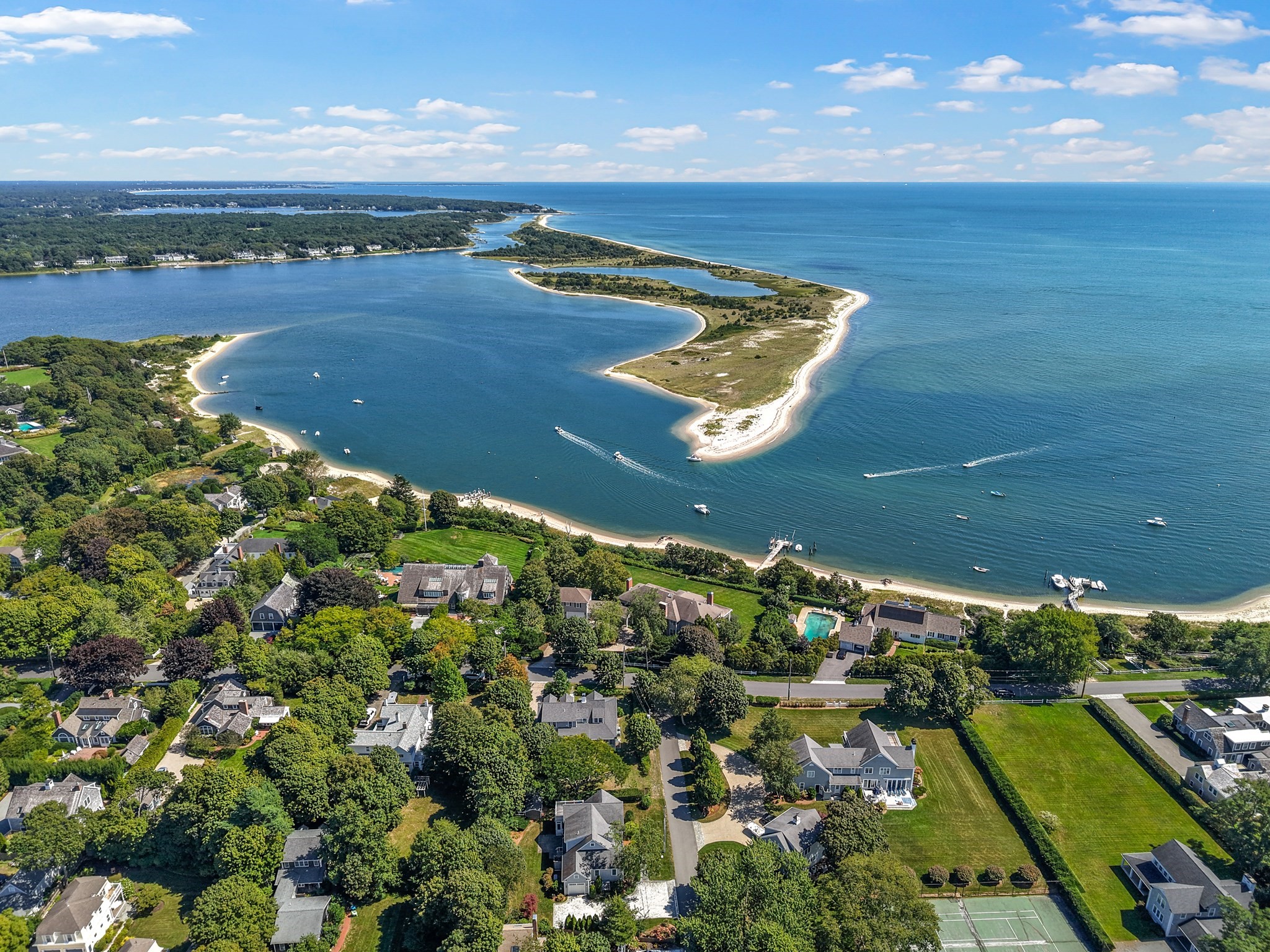 Aerial view of coastal homes beside a bay, with boats and a sandy barrier beach.