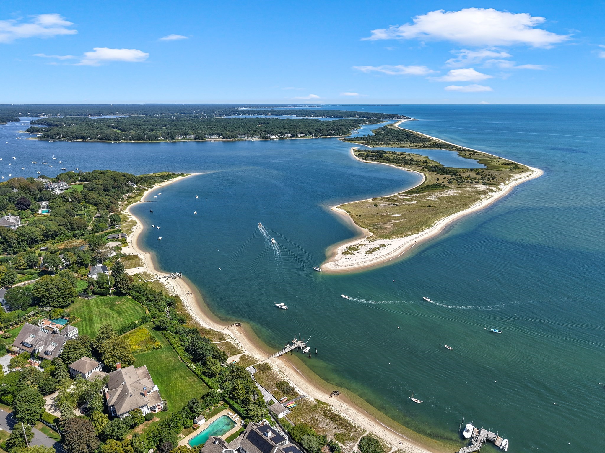 Aerial view of waterfront homes, sandy beaches, and boats along a curving blue inlet.