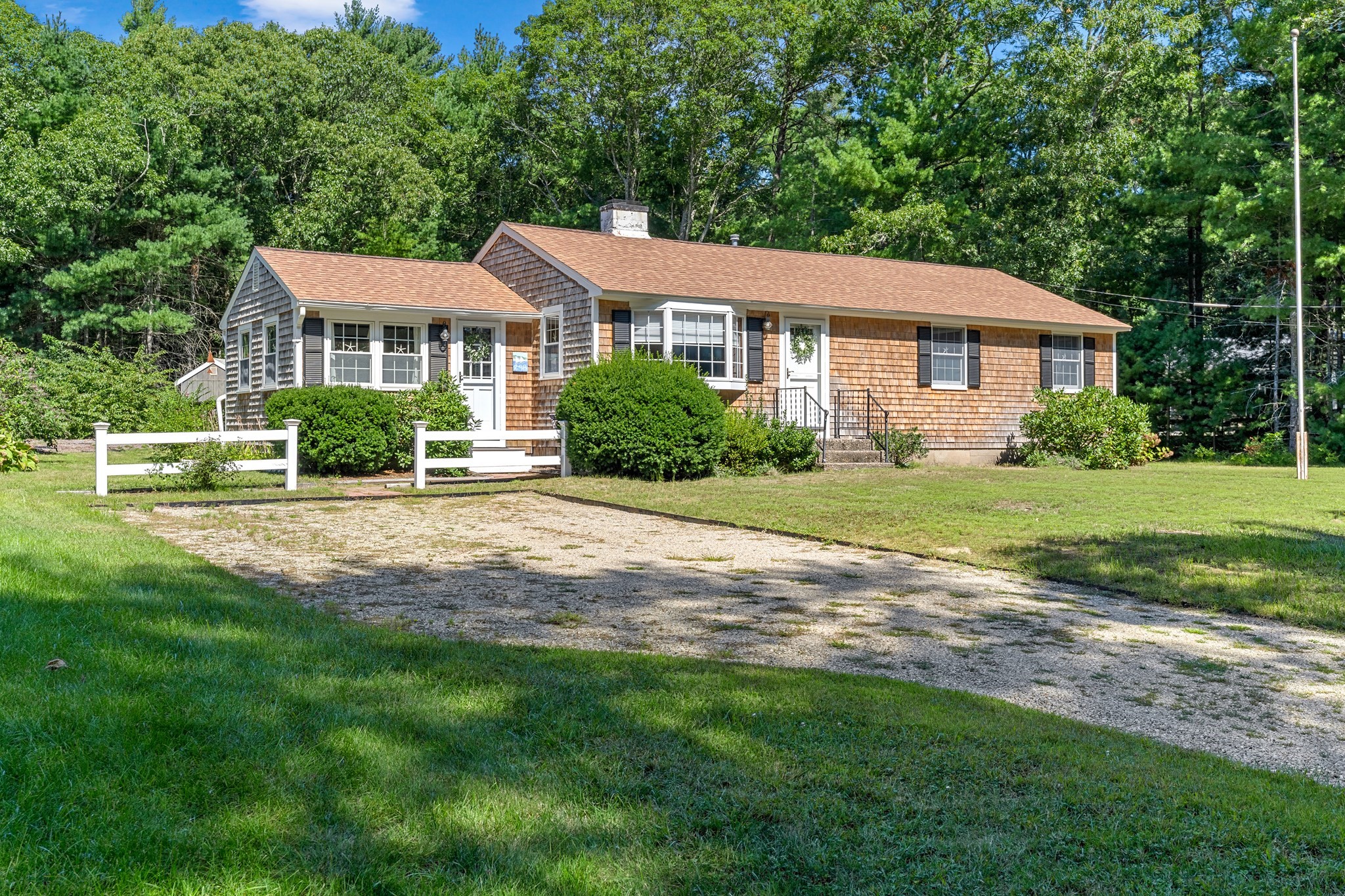 Single-story cedar-shingle home with a gravel driveway and mature trees.