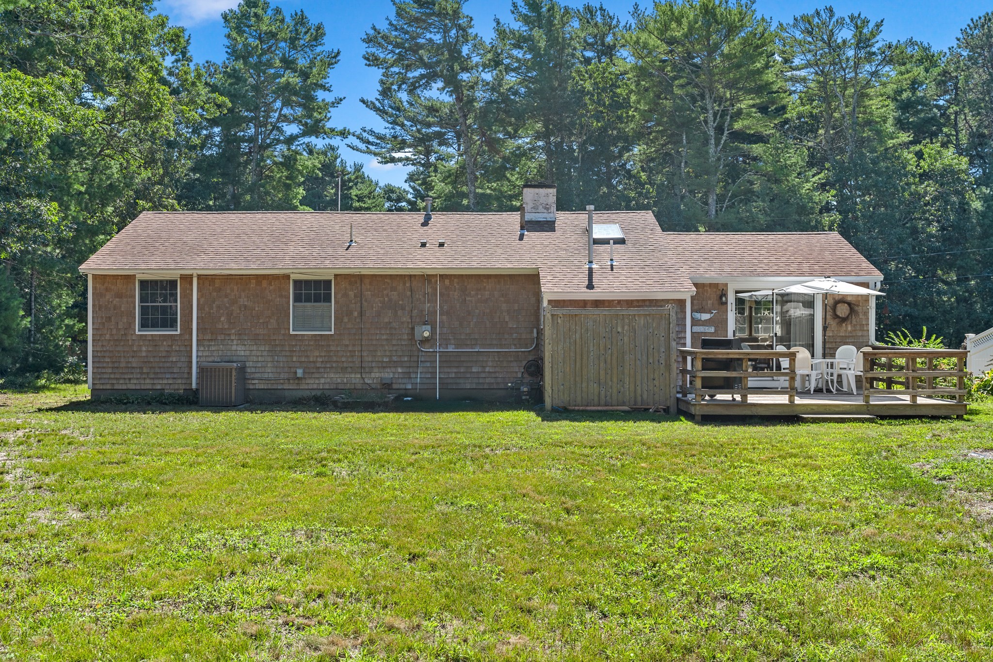 Rear of a shingle-sided house with a furnished wooden deck and a broad lawn.