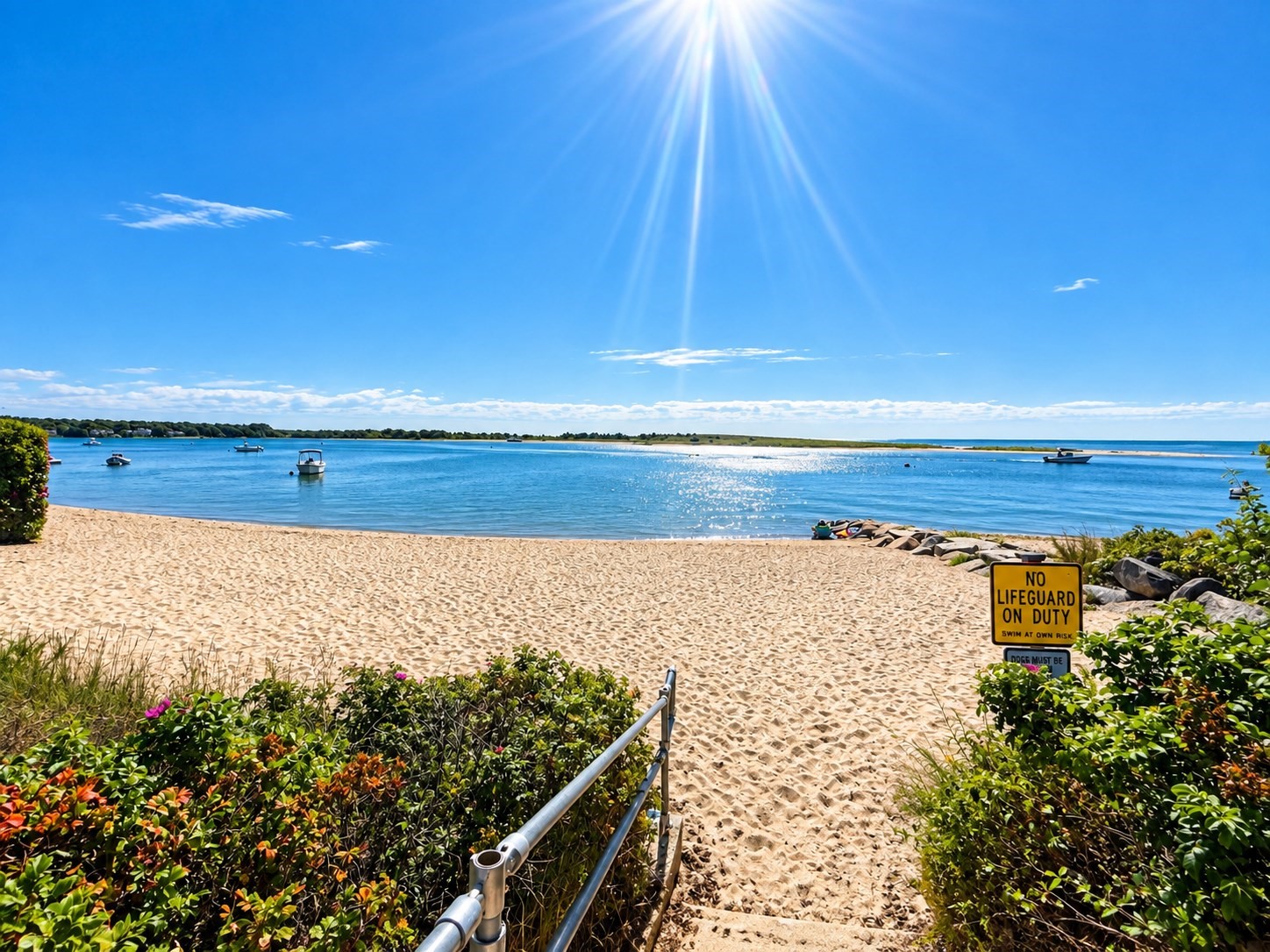Sandy beach access overlooking calm blue water and boats, with a no-lifeguard warning sign.