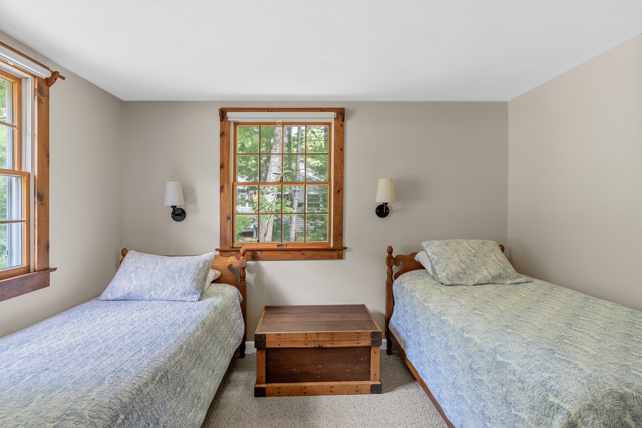 Bedroom with two single beds and a wooden chest between them, with trees visible through the windows.