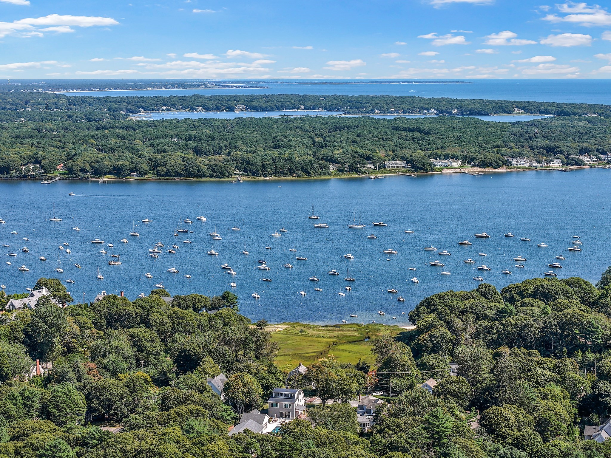 Aerial view of a wooded coastal neighborhood overlooking a boat-filled bay.