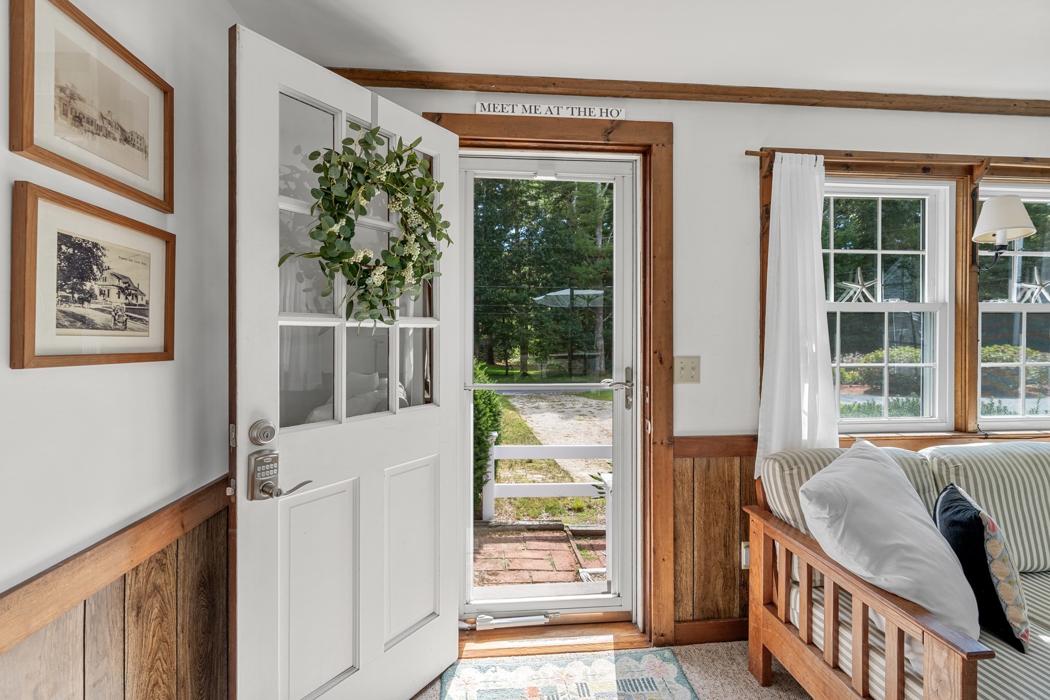 Living room with an open white front door, wood trim, and a striped daybed by the windows.