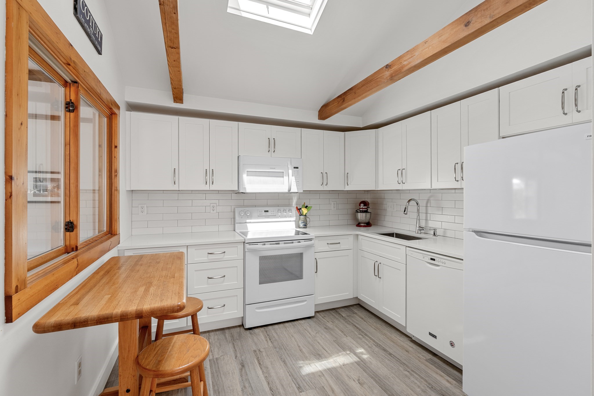 Bright white kitchen with a skylight, exposed wood beams, and a built-in counter with stools.