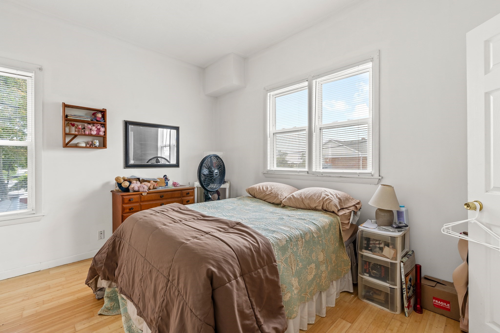 Bedroom with a teal patterned bedspread, wooden dresser, and three windows with blinds.