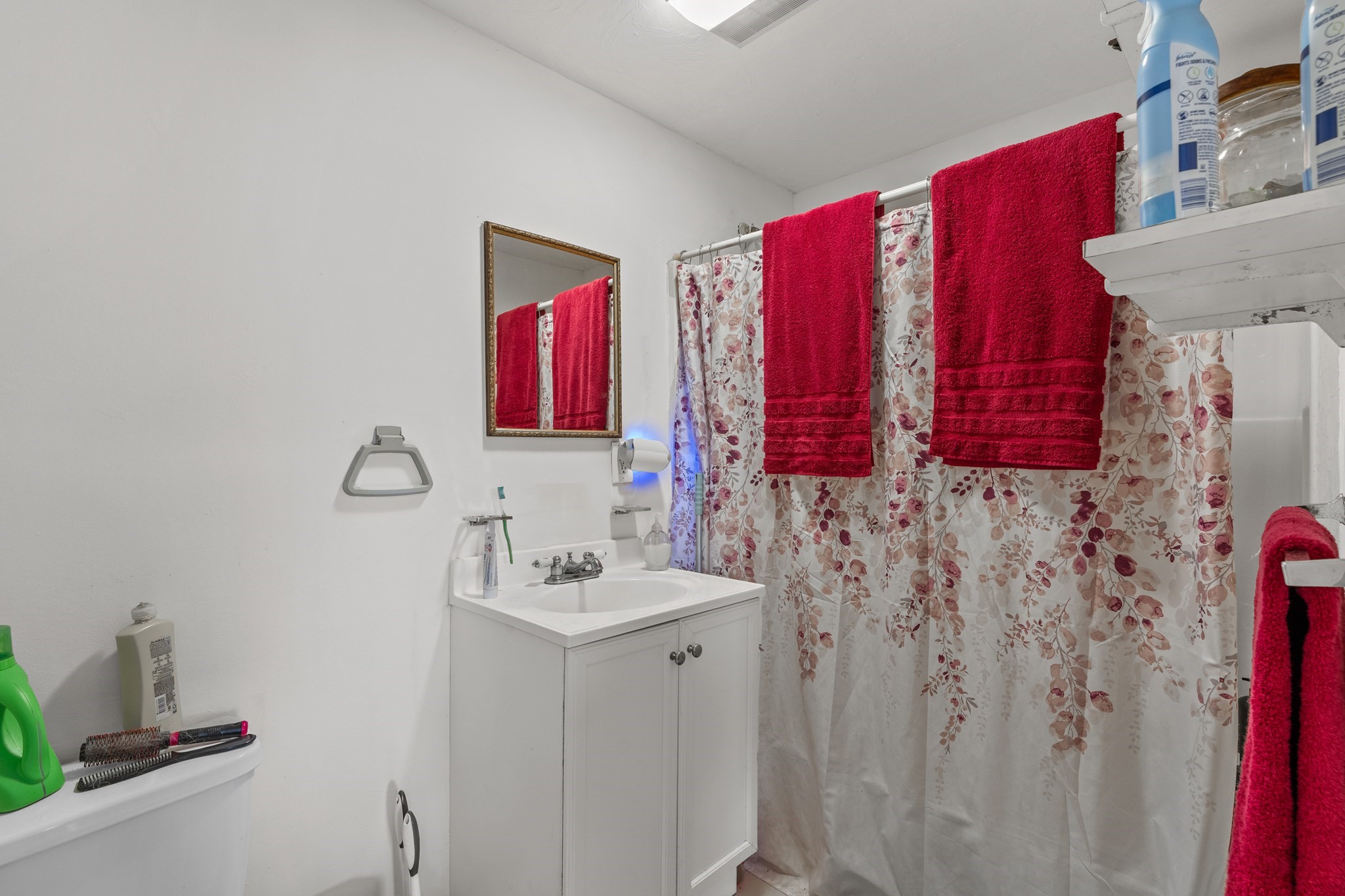 Bathroom with a white vanity, floral shower curtain, and bright red towels.