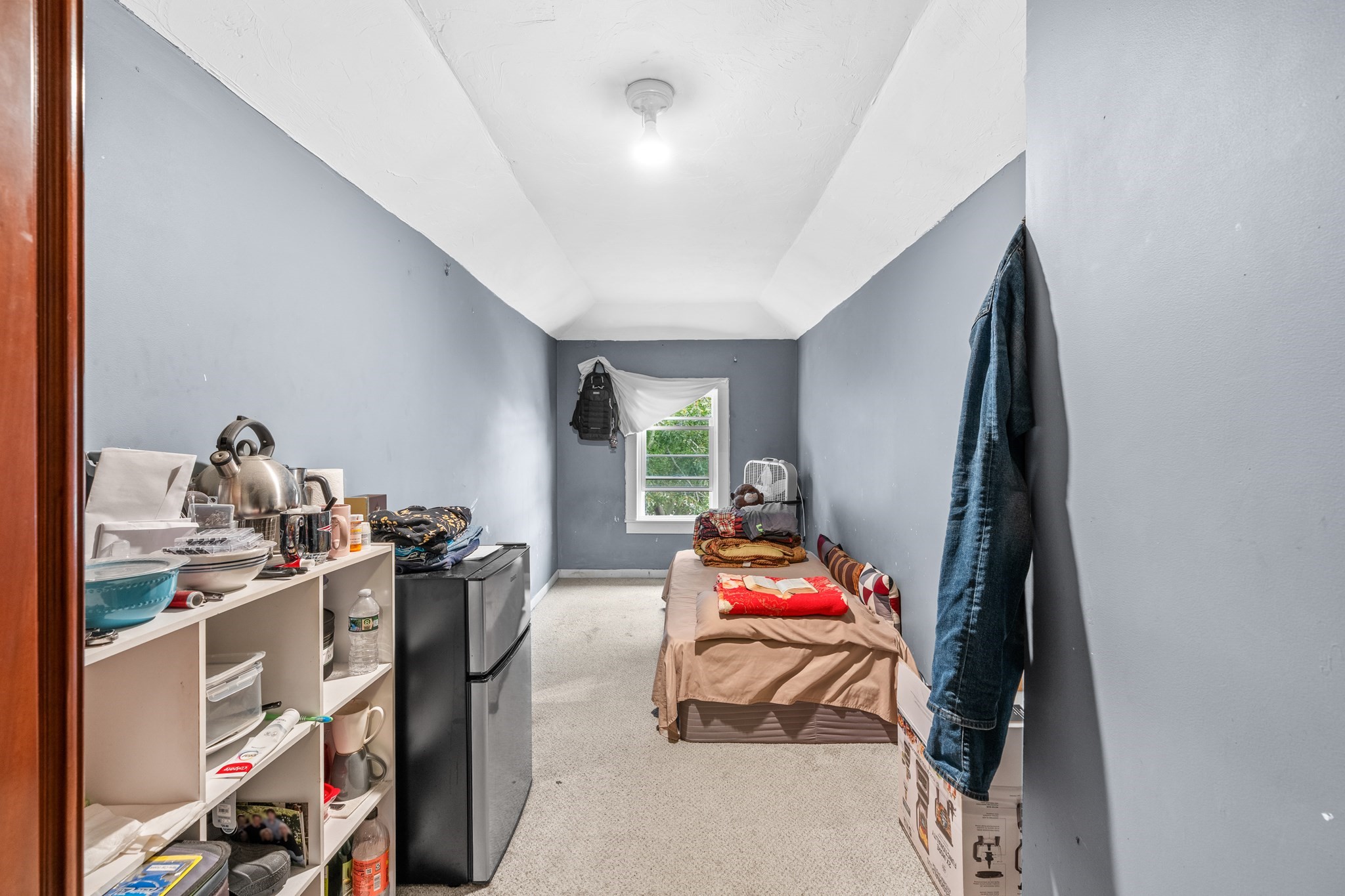 Narrow bedroom with a single bed, open shelving, and a compact refrigerator.