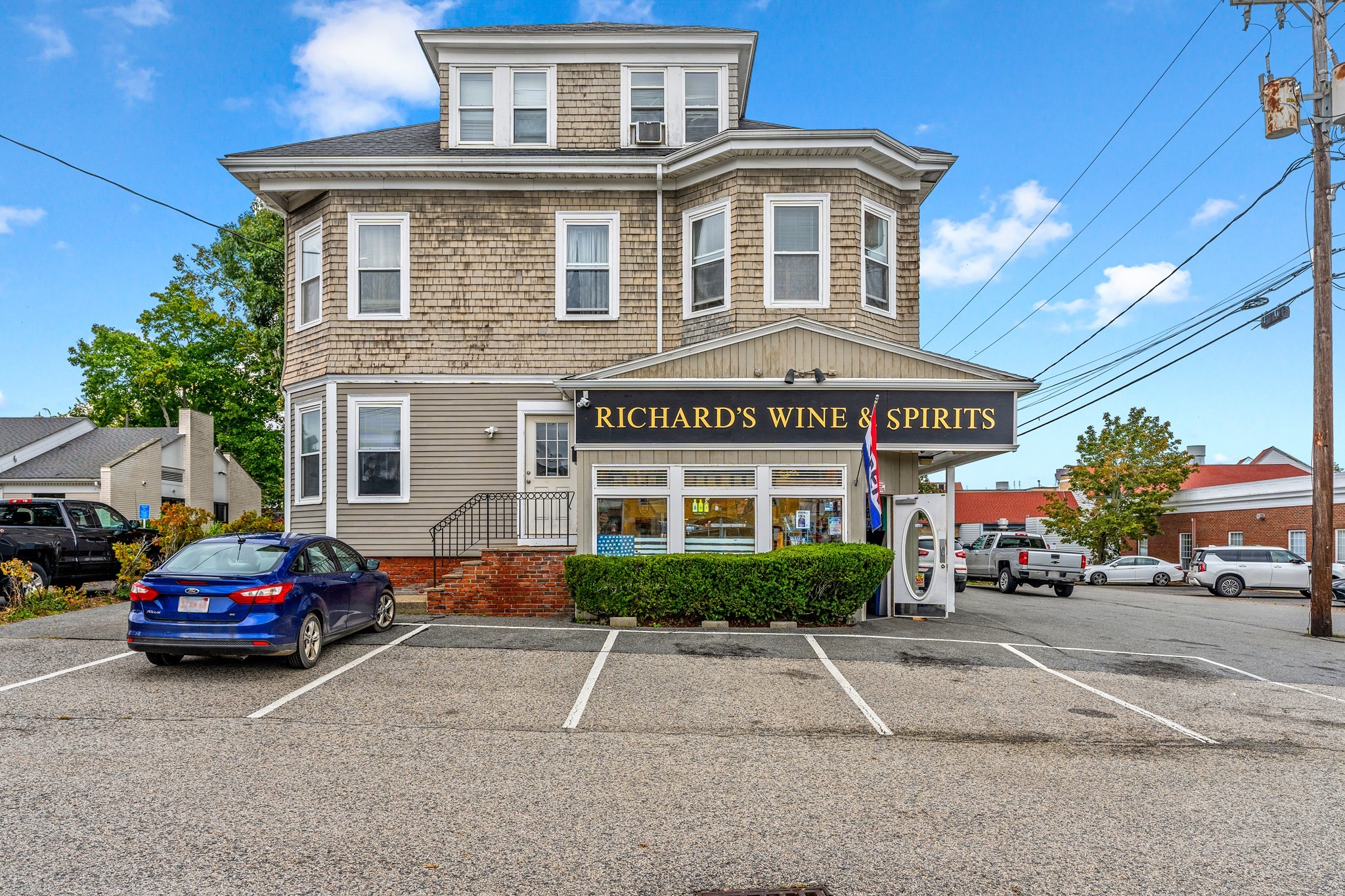 Three-story shingle-sided building housing Richard’s Wine & Spirits, with a storefront and parking lot.