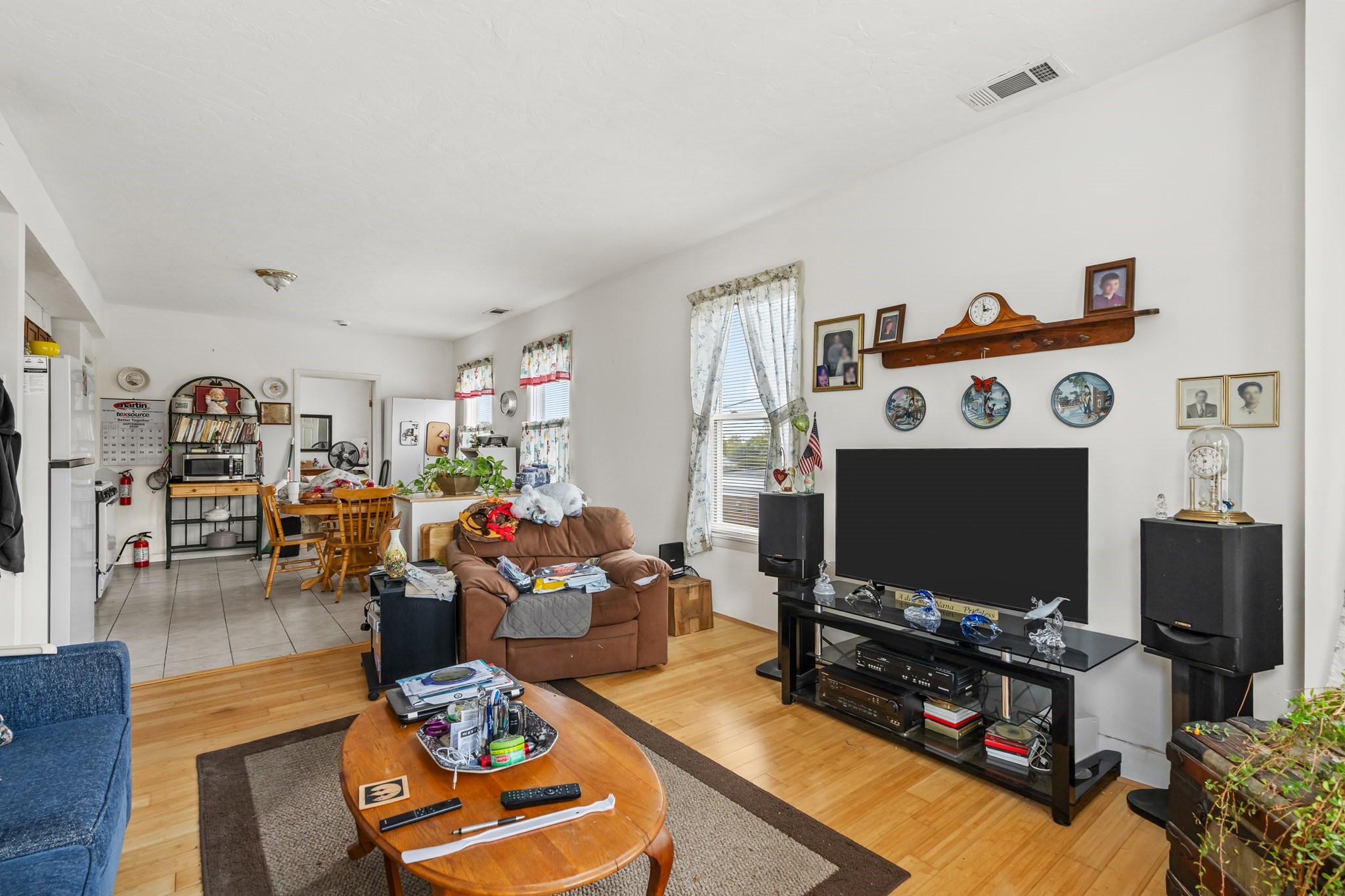Living room with hardwood floors, a brown sofa, and a large television beside an open dining area and kitchen.