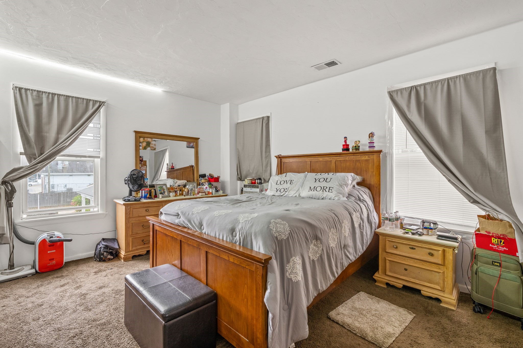 Furnished bedroom with a wooden bed, gray patterned bedding, and gray curtains over two windows.