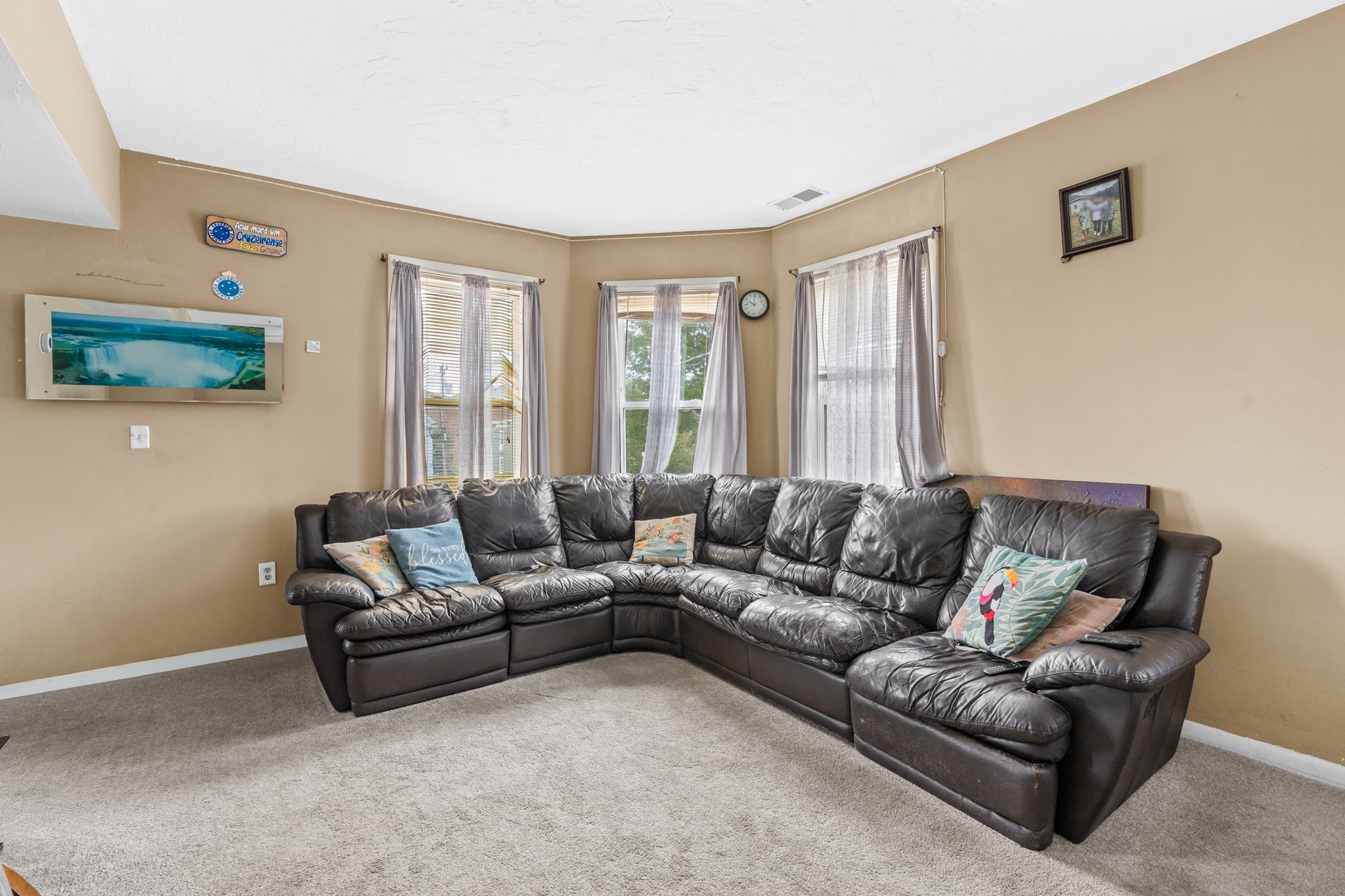 Living room with a large dark leather sectional beneath three curtained windows.