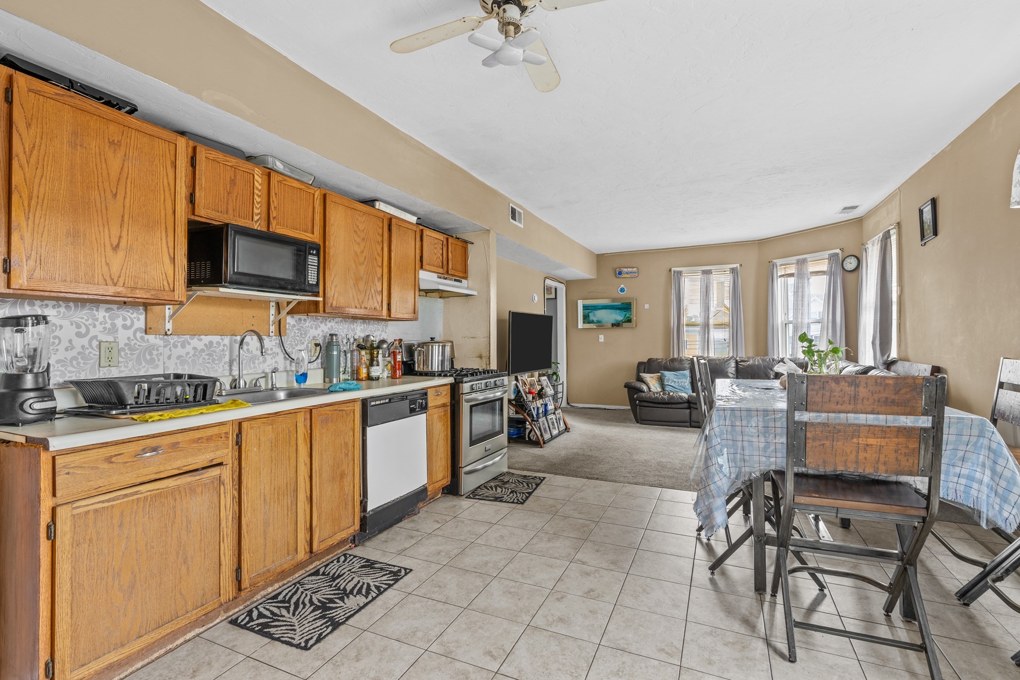Open-plan kitchen and living area with wood cabinets, tiled floors, and a dining table.