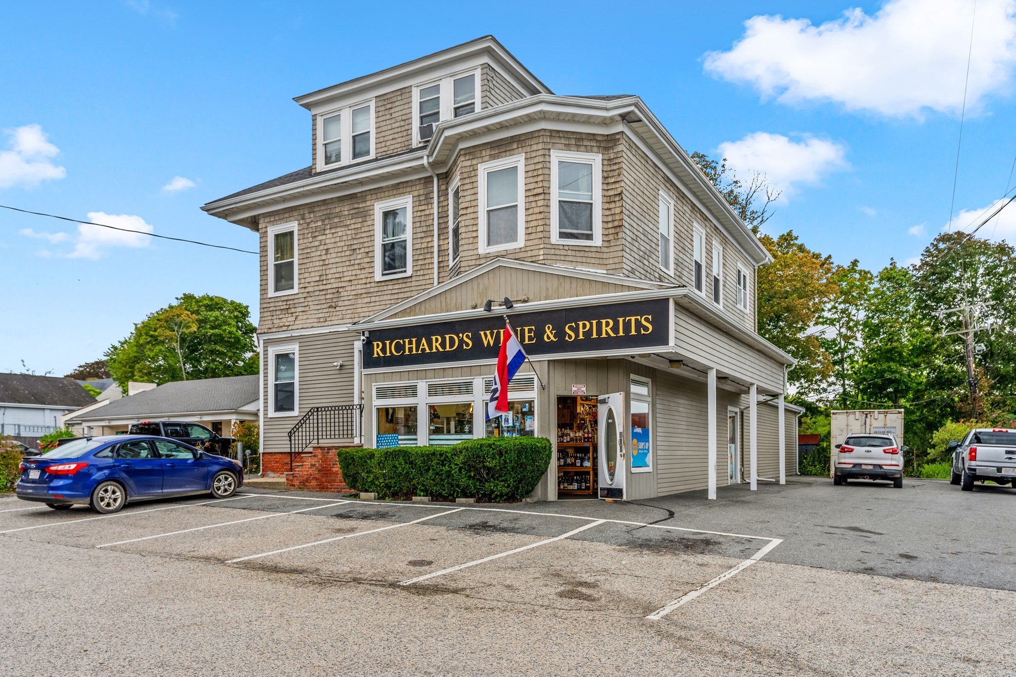 Multi-story shingle-sided wine and spirits store with a black-and-gold storefront sign and parking lot.