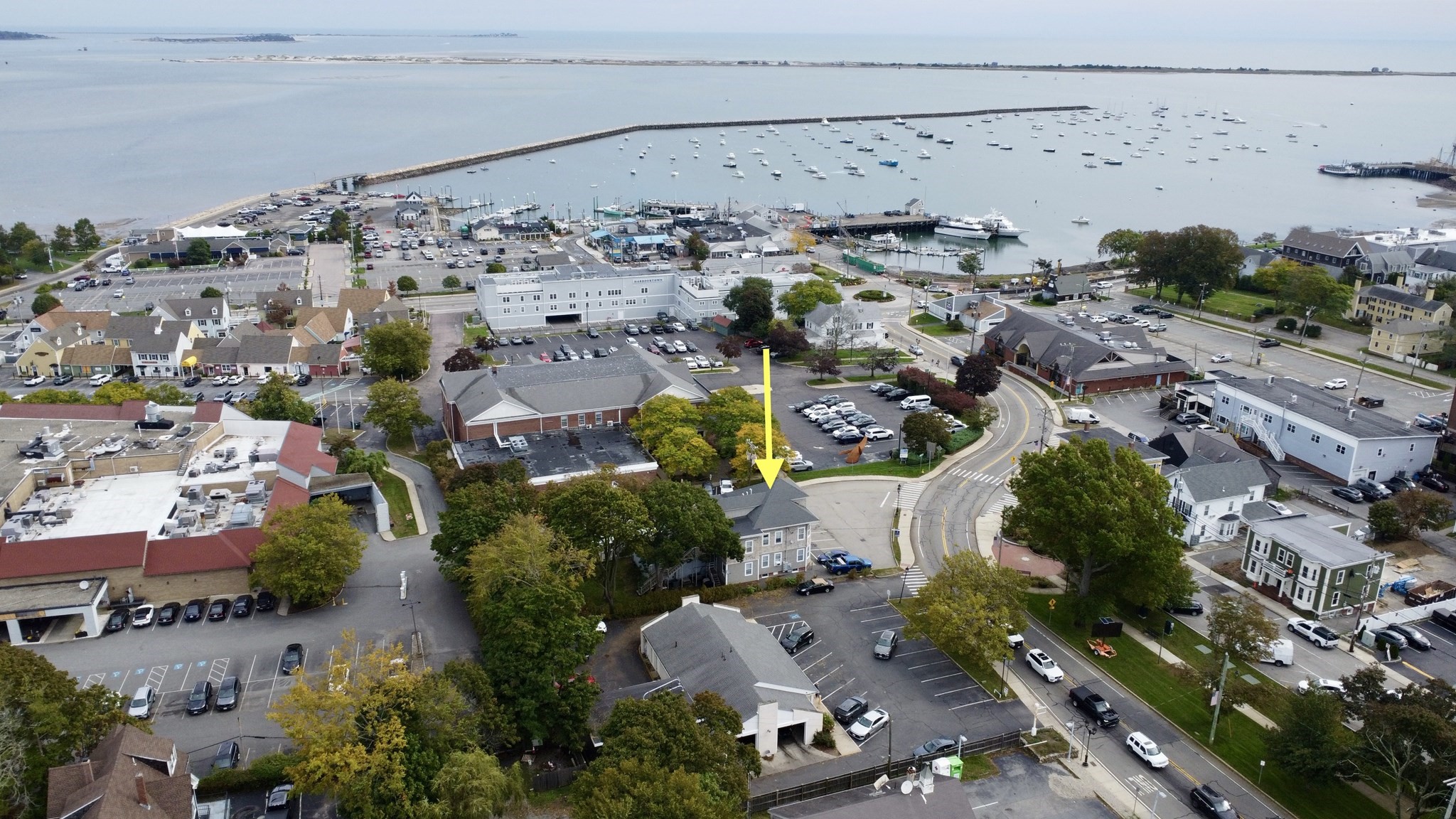 Aerial view of the marked property near a boat-filled harbor and curved breakwater.