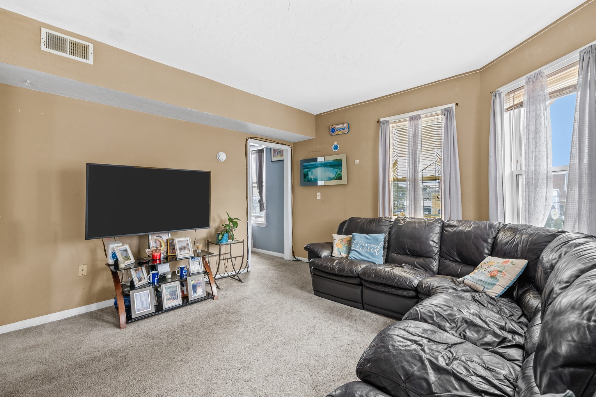 Living room with a black leather sectional, beige carpet, and tall curtained windows.
