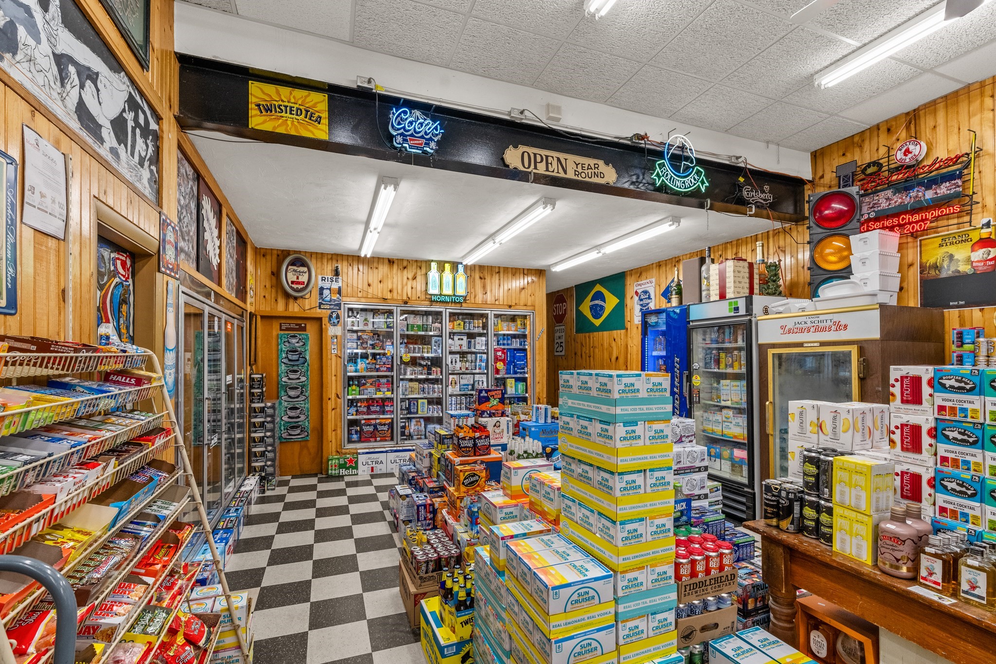 Liquor store interior with wood paneling, checkered floors, and stacks of boxed beverages.