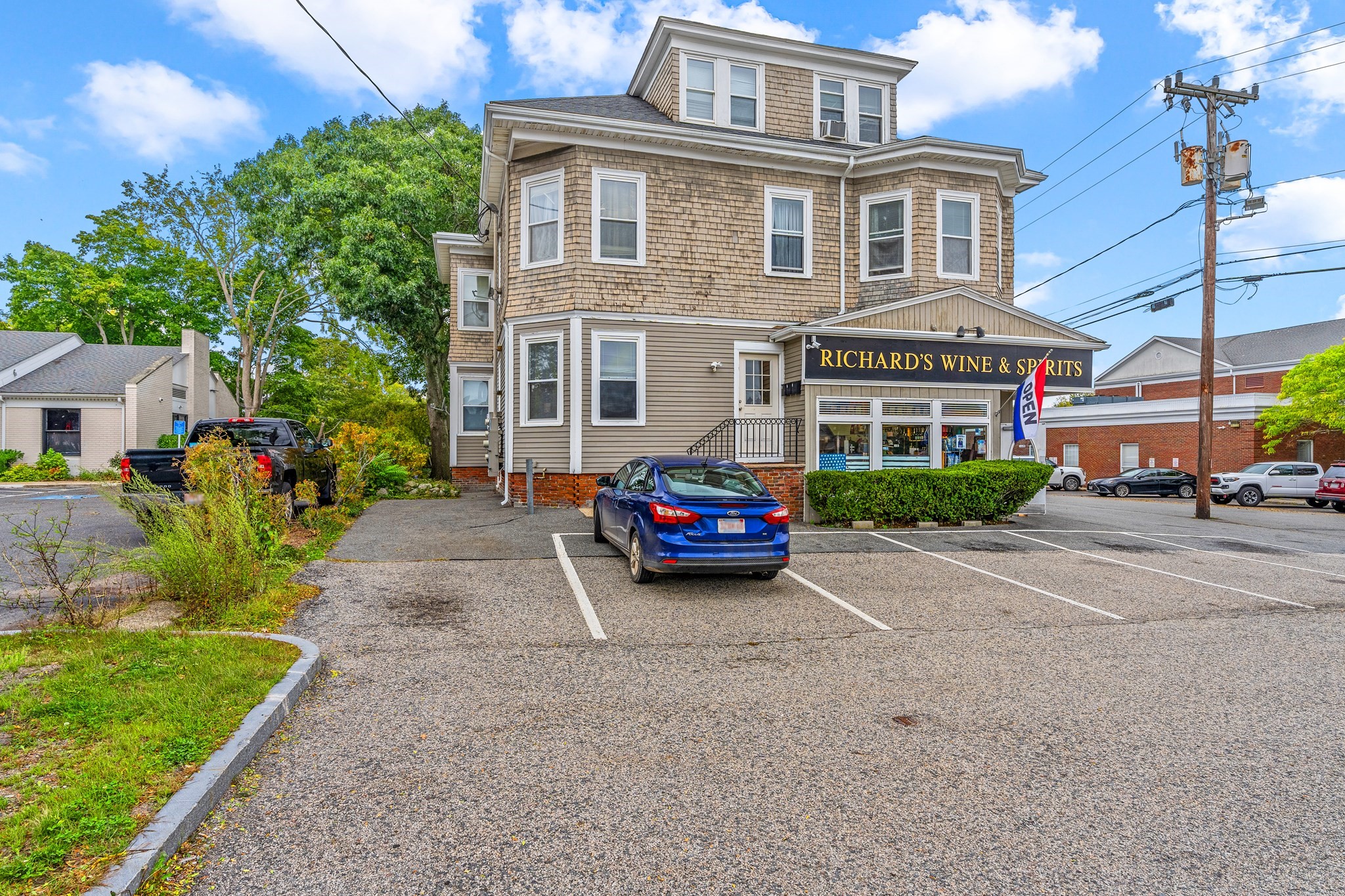Three-story shingle-sided building with a wine and spirits storefront and parking lot.