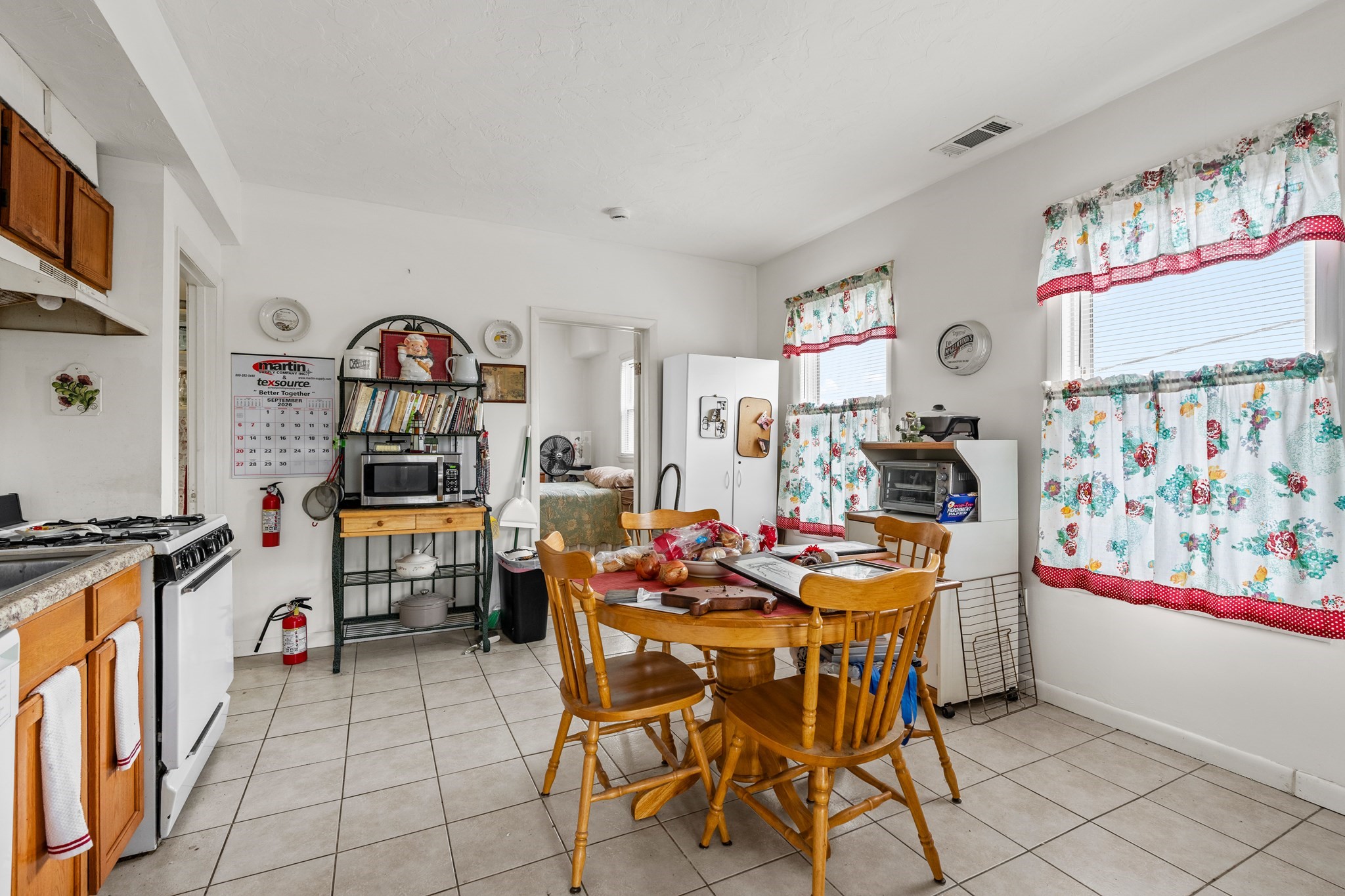 Kitchen and dining area with a round wooden table, white appliances, and floral curtains.