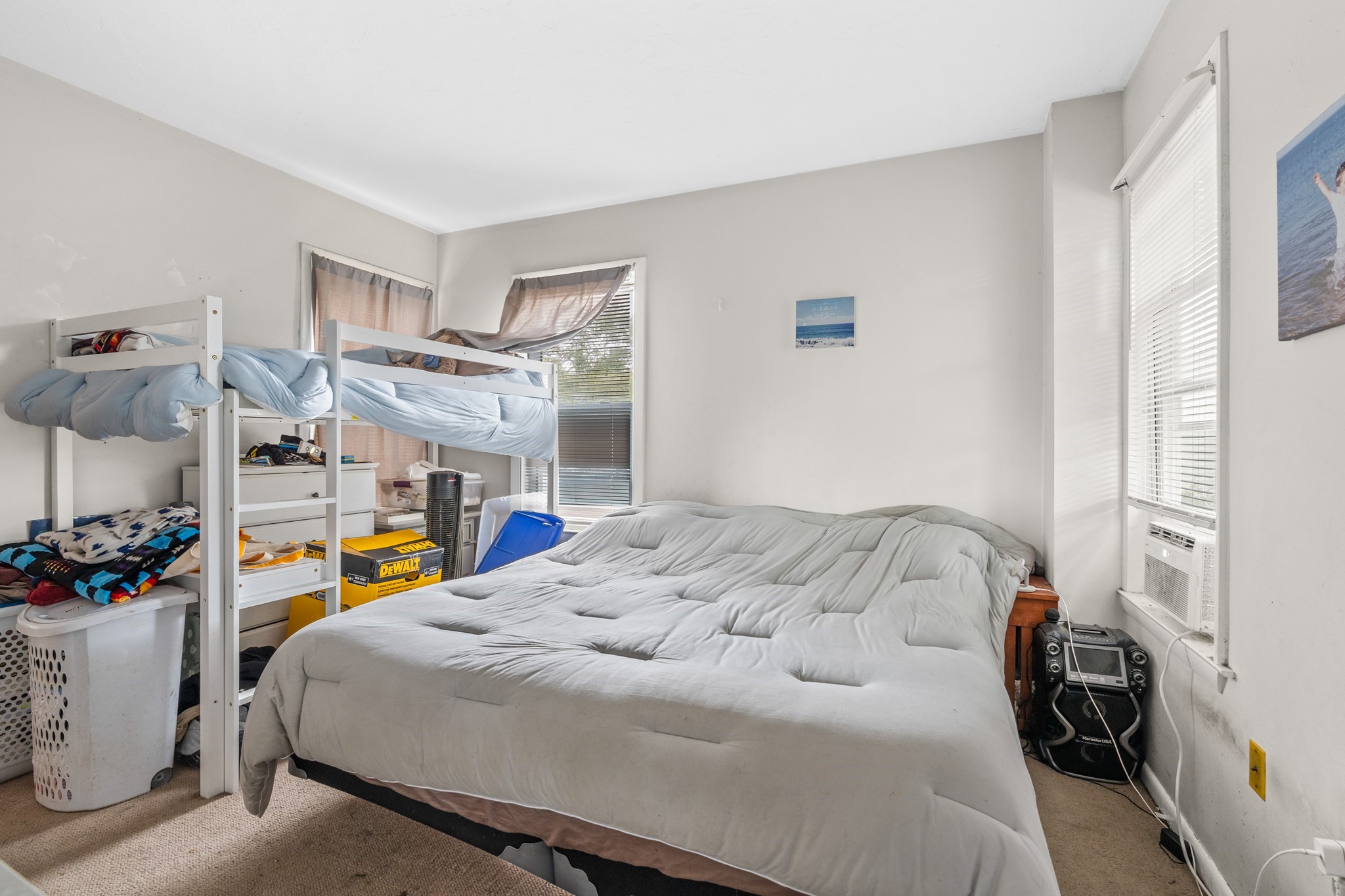 Bedroom with a large bed, white bunk bed, and cluttered storage beside several windows.