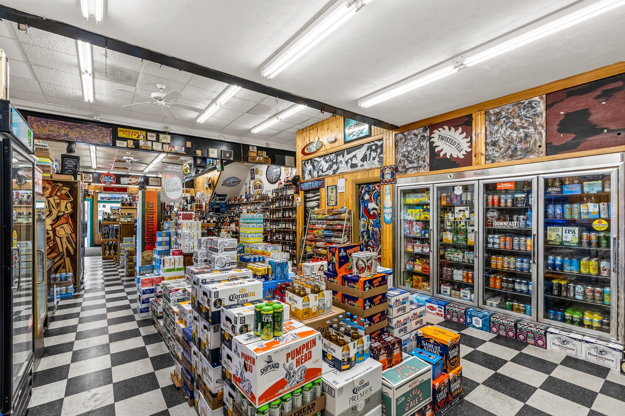 Liquor store interior with stocked beer coolers, stacked cases, and a black-and-white checkerboard floor.