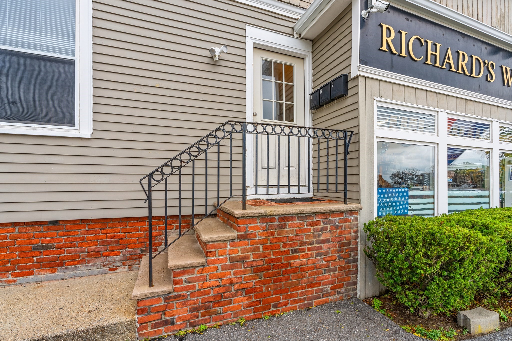Commercial building entrance with brick steps, black iron railing, and a cropped storefront sign.