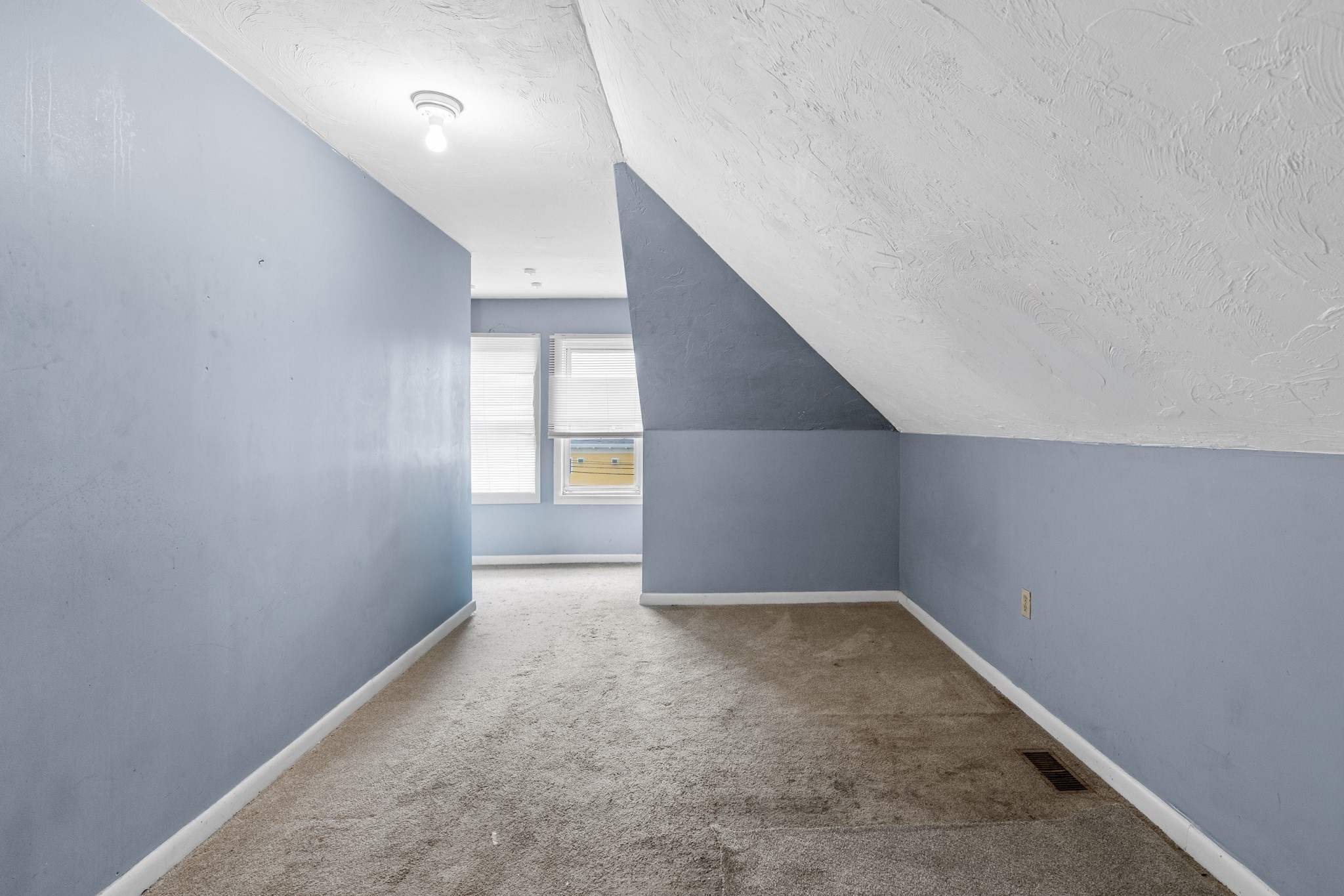 Empty carpeted room with blue-gray walls, a sloped ceiling, and two windows with blinds.