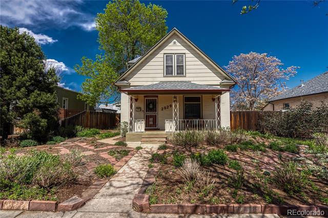 House with a covered porch, brick walkway, landscaped yard, and flowering tree.