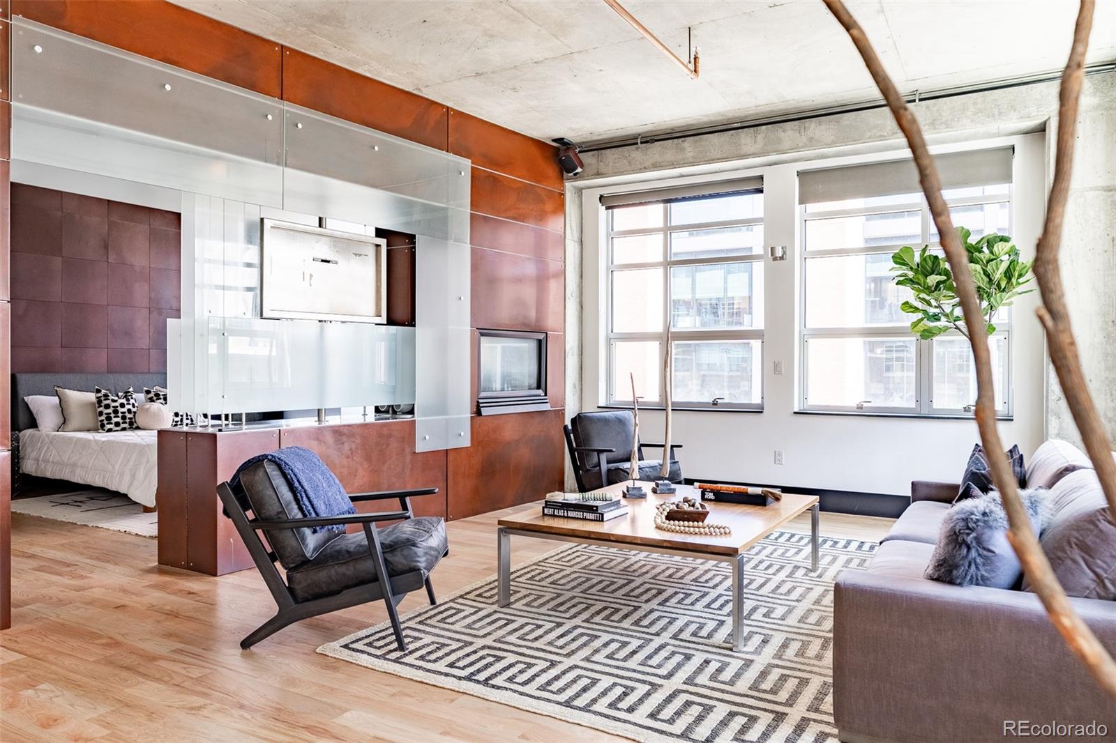 Modern condo living room with glass-partitioned bedroom, copper panels, and large windows.