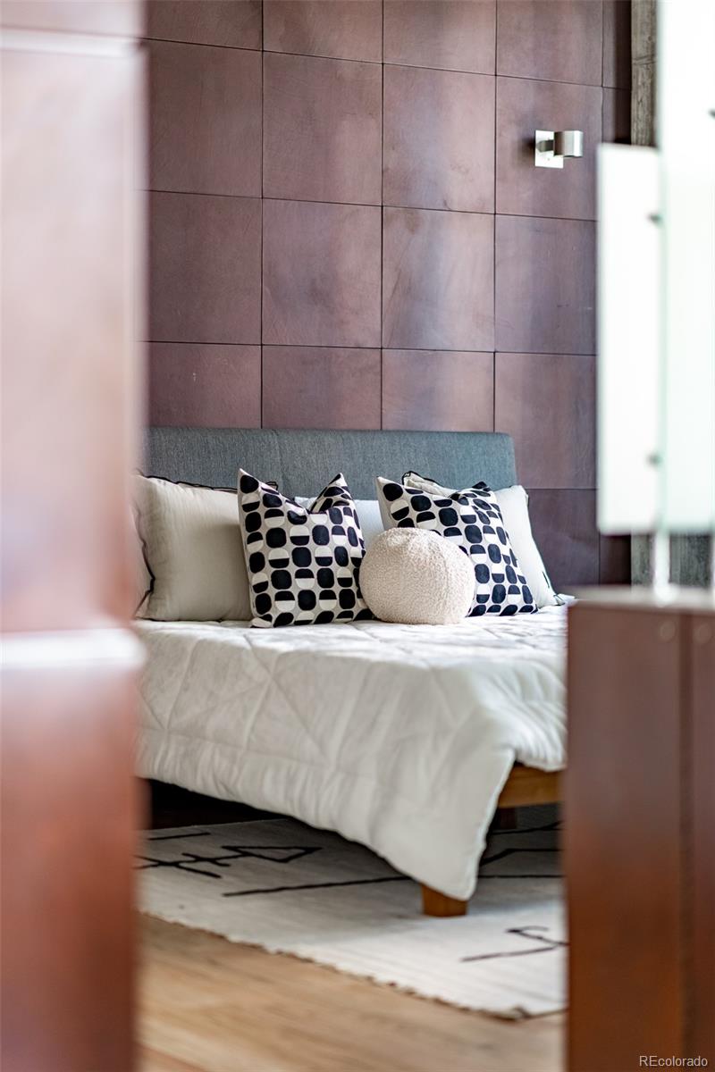 Furnished bedroom with a white bed and patterned pillows against a mauve paneled wall.
