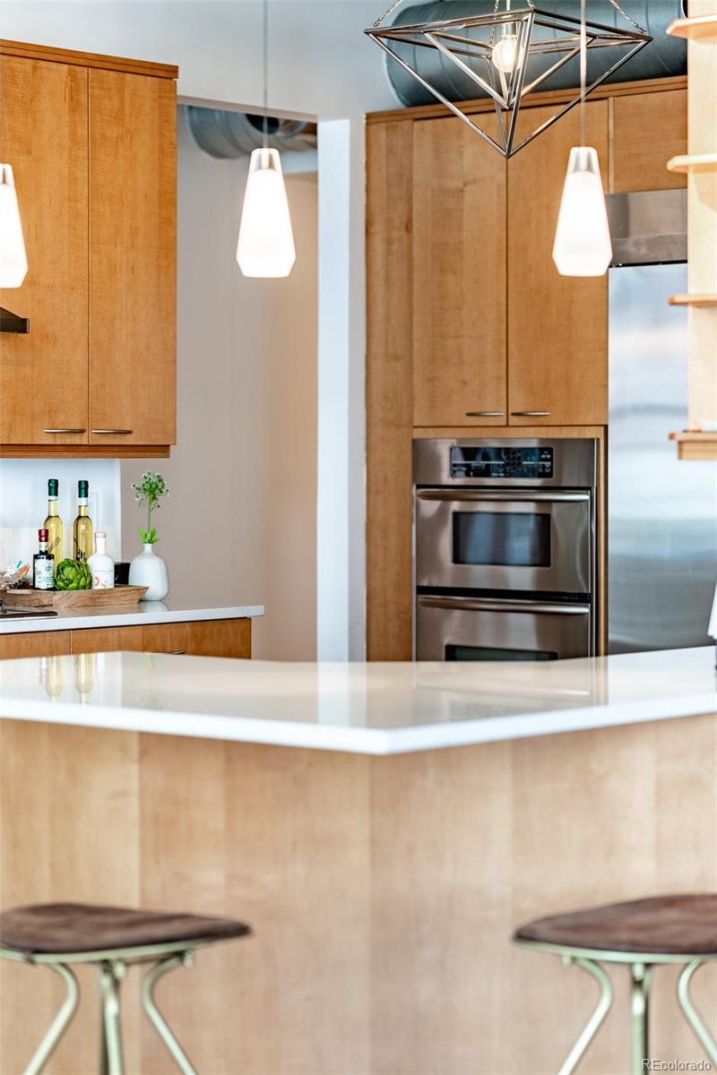 Condo kitchen with a white island, warm wood cabinets, stainless steel appliances, and pendant lights.