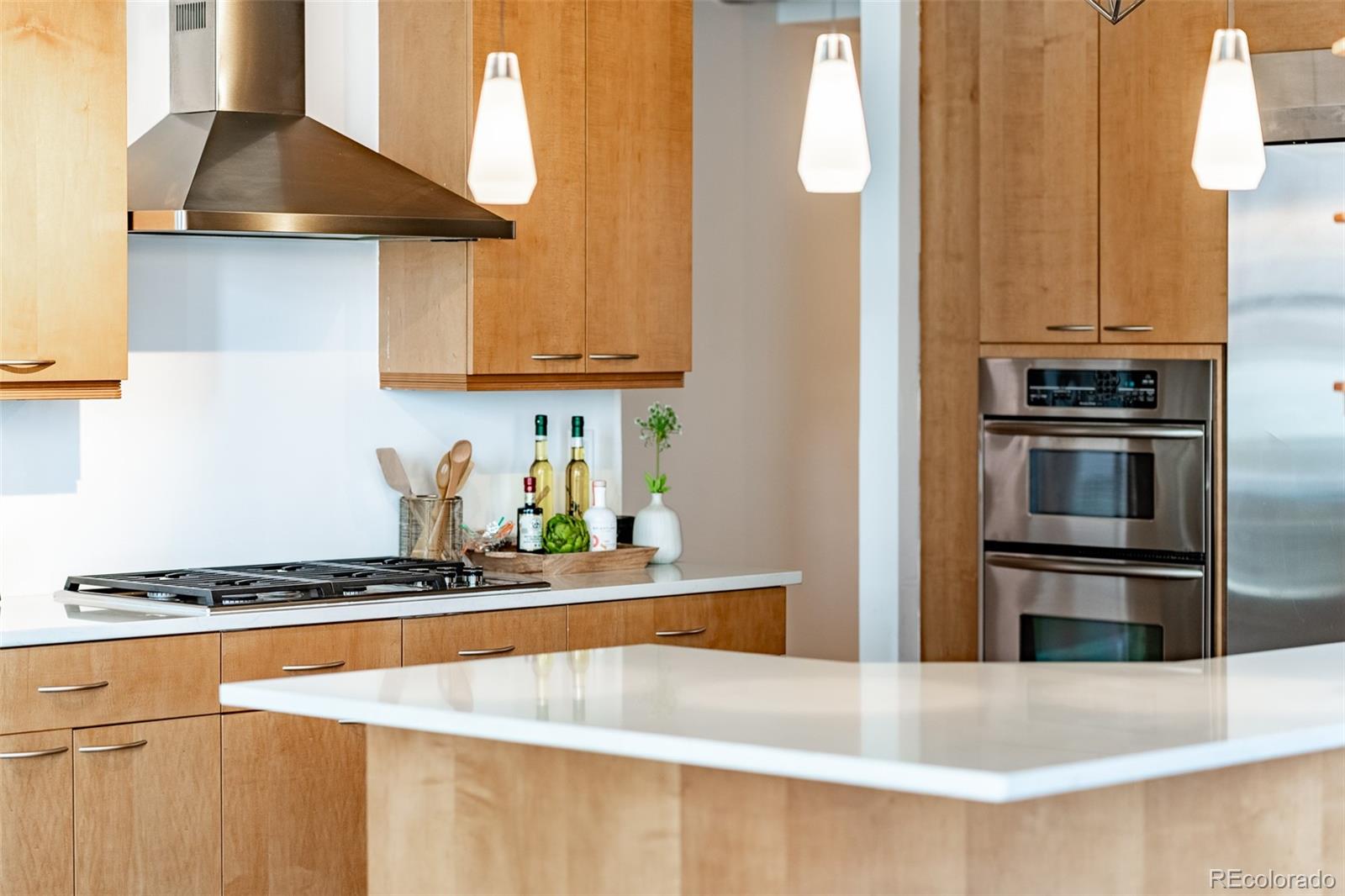 Modern kitchen with warm wood cabinets, a white island, gas cooktop, and stainless steel double oven.