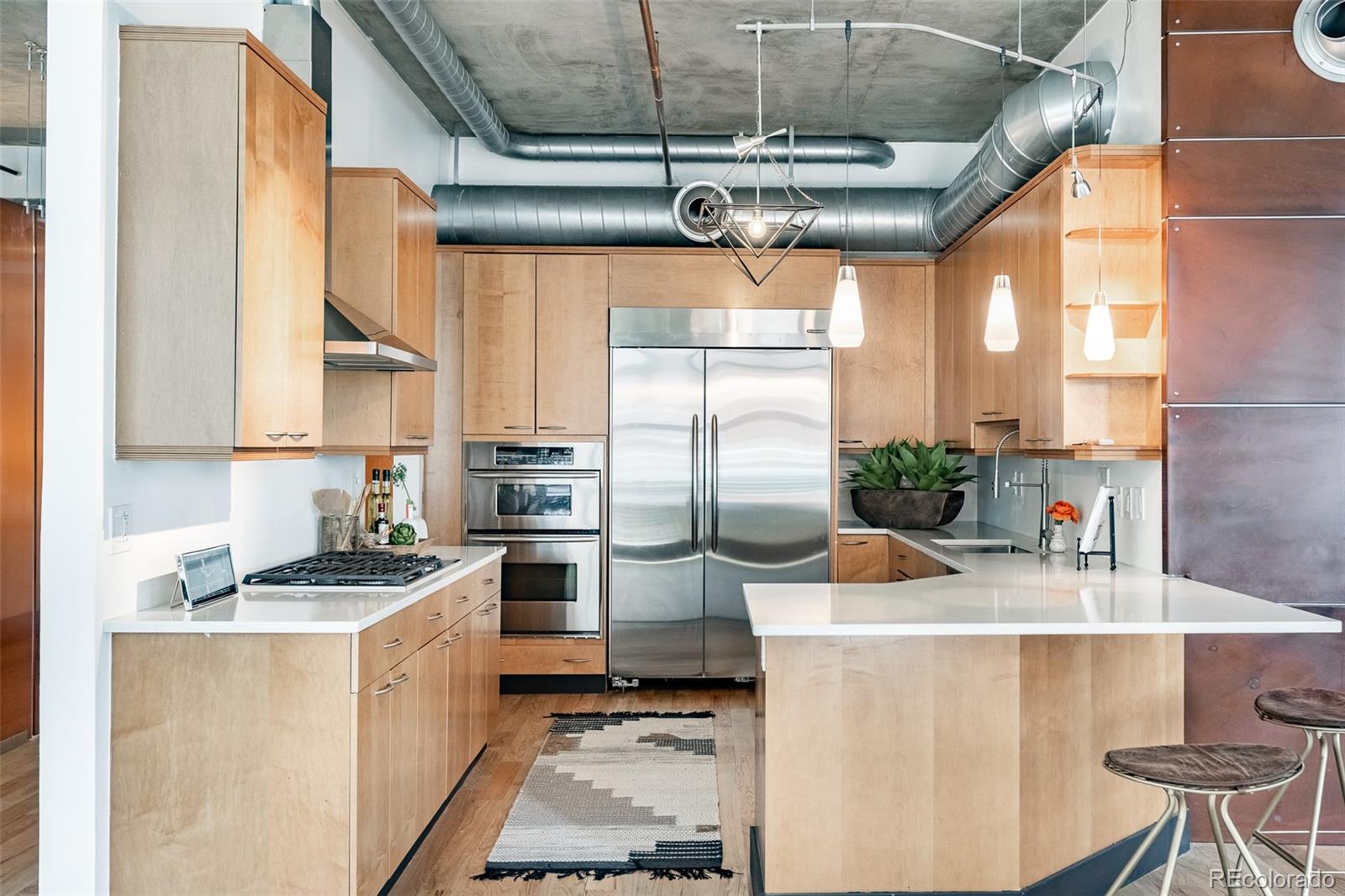 Condominium kitchen with light wood cabinets, stainless steel appliances, and a large white island.