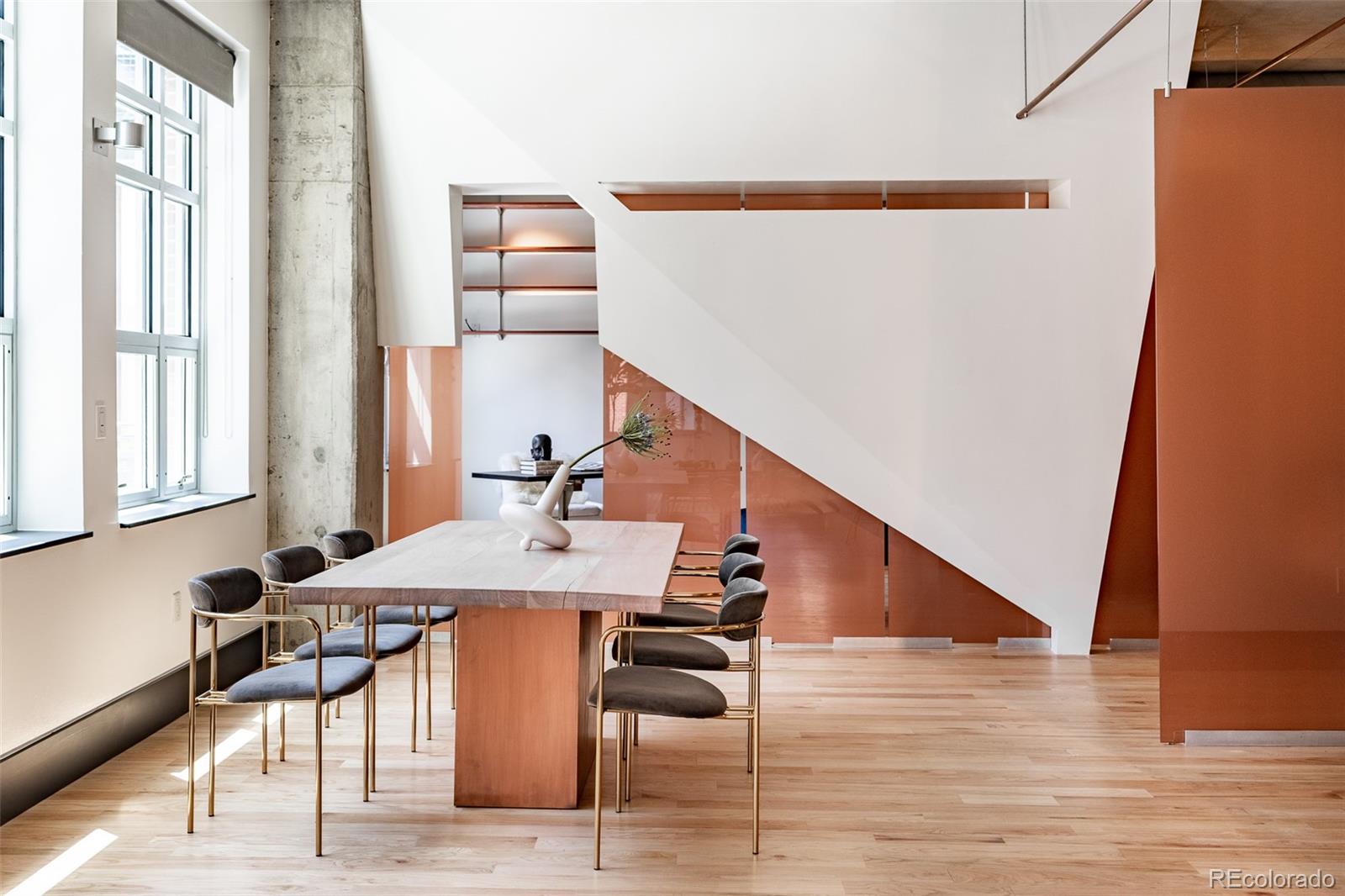Modern loft dining area with a long wood table, orange glass partitions, and a dramatic white staircase.