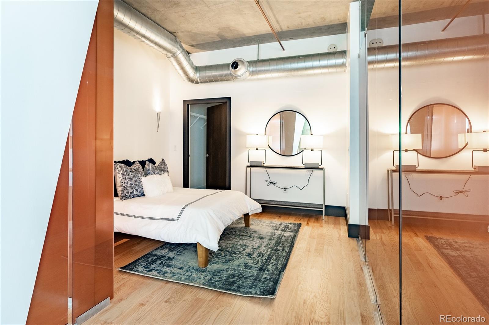 Bedroom with a glass partition, exposed ductwork, and a bed on a patterned rug.