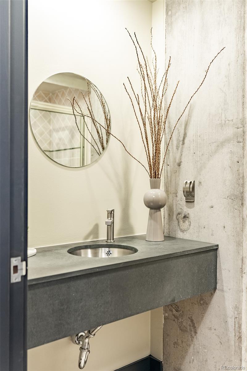 Powder room vanity with a round mirror, dark stone counter, and vase of branches.