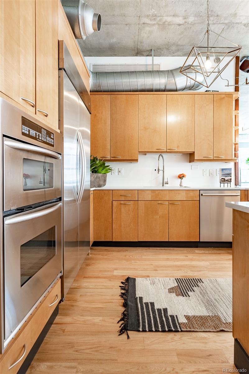 Modern kitchen with light wood cabinetry, stainless steel appliances, and exposed ceiling ductwork.