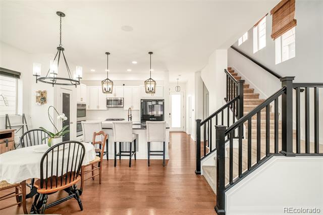 Open kitchen and dining area with a central island, warm wood floors, and a staircase.