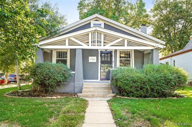 Gray bungalow with a white gabled porch, front walkway, mature trees, and landscaped shrubs.