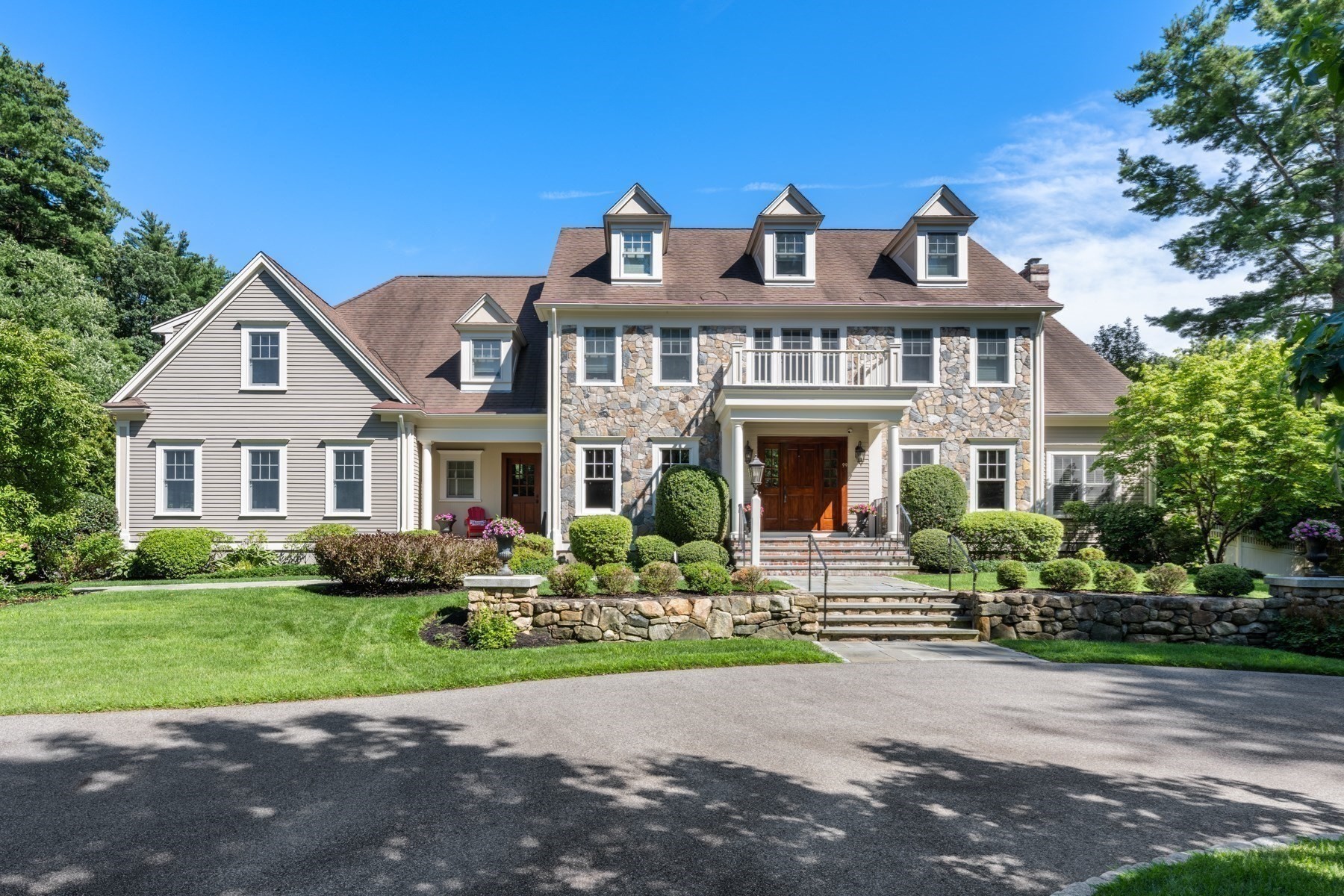 Large stone-and-siding home with roof dormers, a landscaped lawn, and a stone retaining wall.