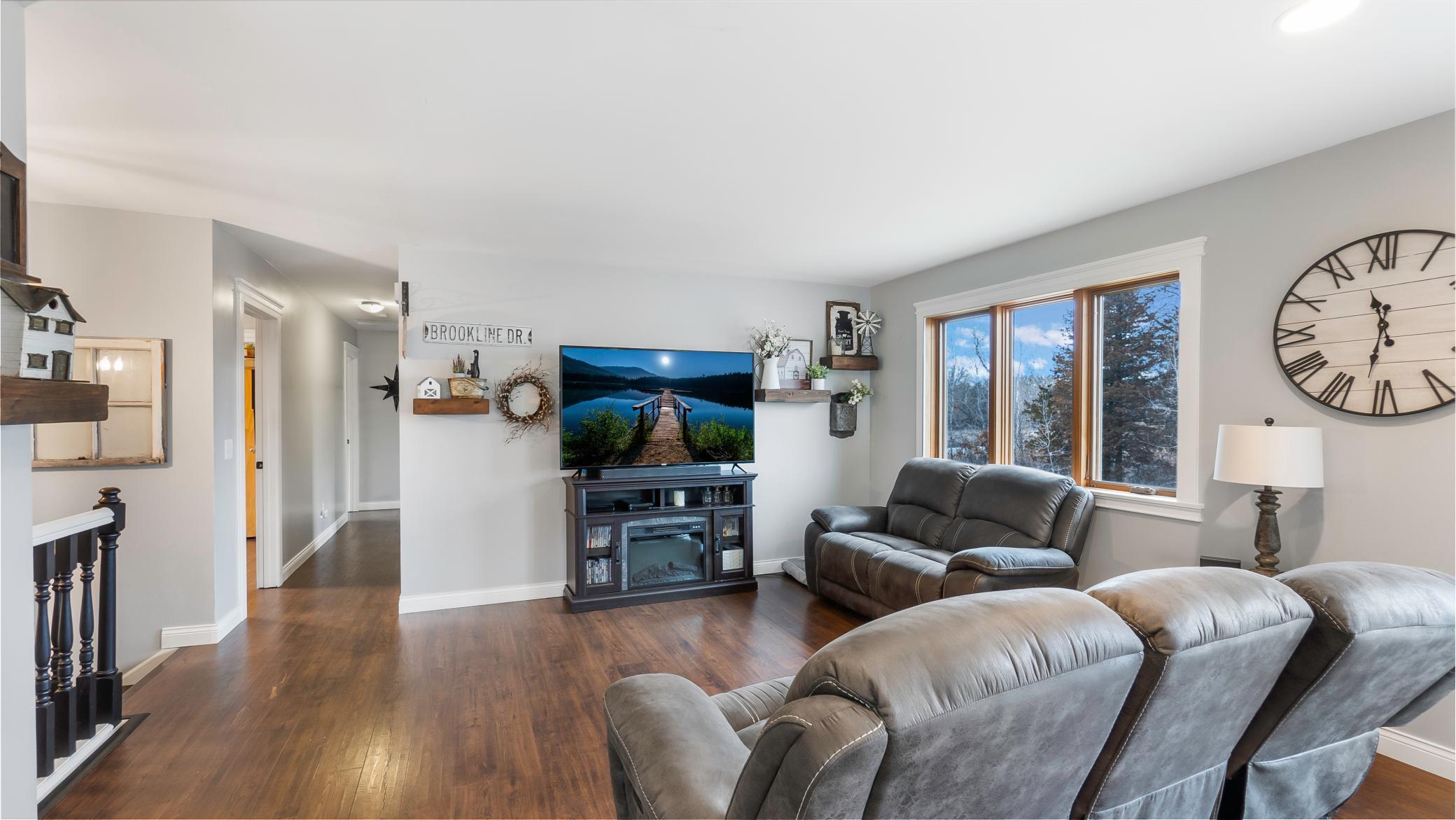 Living room with leather seating, dark wood floors, and large windows overlooking snow-dusted trees.