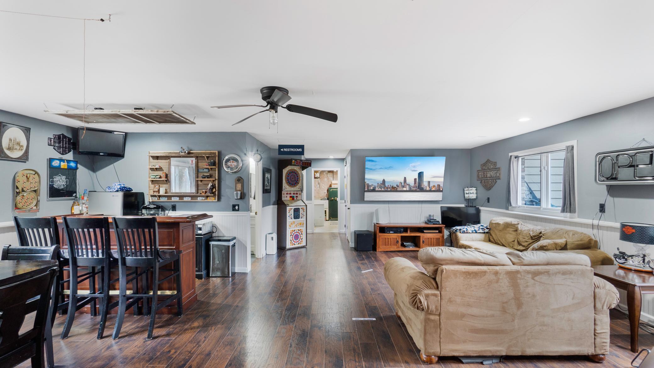 Recreation room with a dark-wood bar, dart machine, and tan sectional sofa.